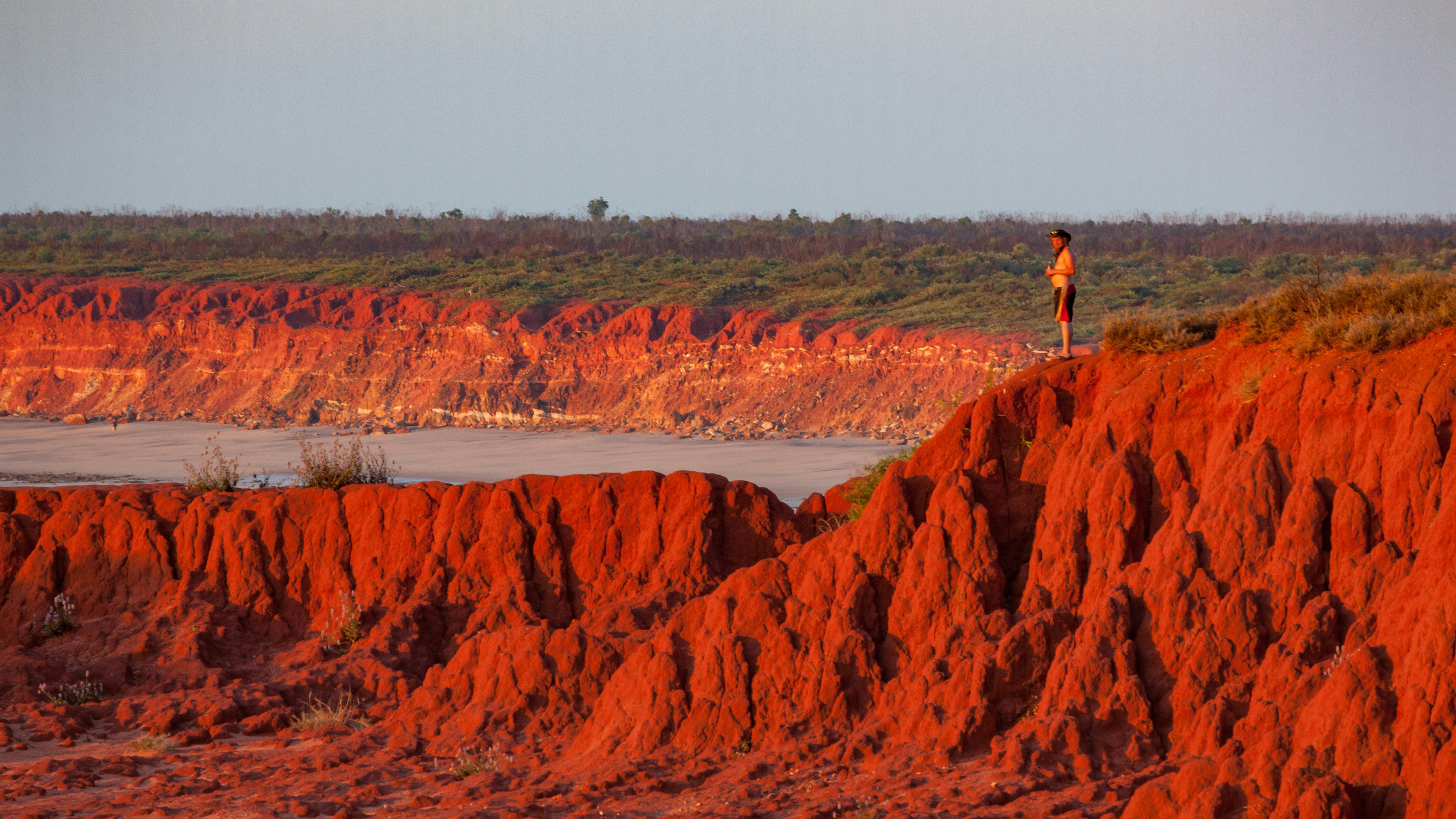 Man standing on top of the Red Pindan Cliffs at sunset, James Price Point, Western Australia.