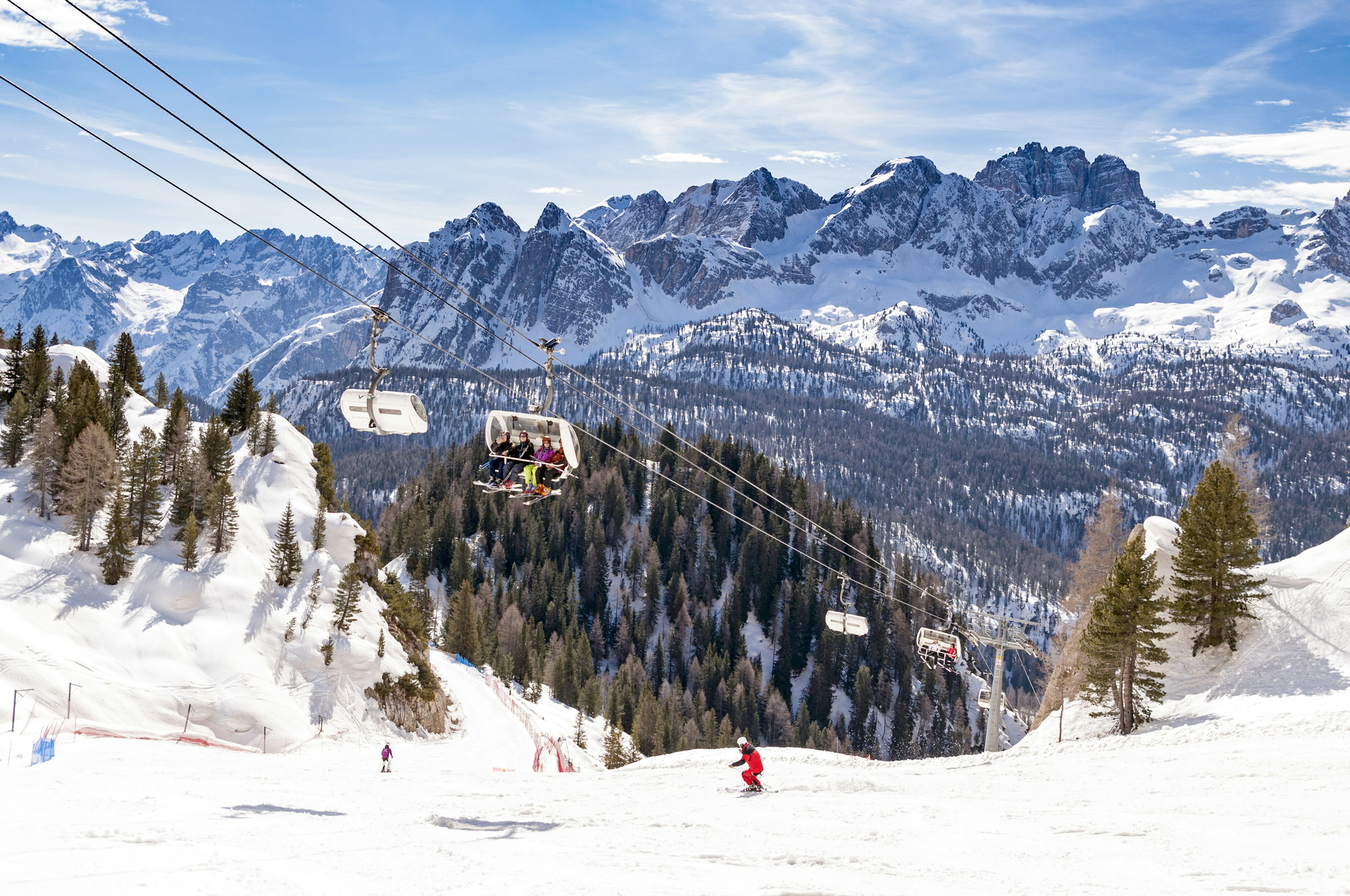 Skiers on the snow-covered slopes with ski lifts carrying other skiers to the top of the piste