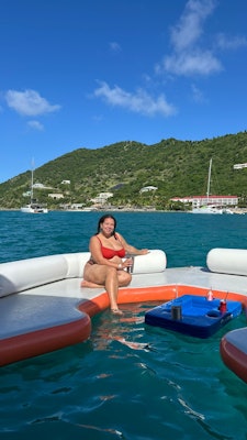 A woman sits on a floating bench with one foot dangling in the ocean