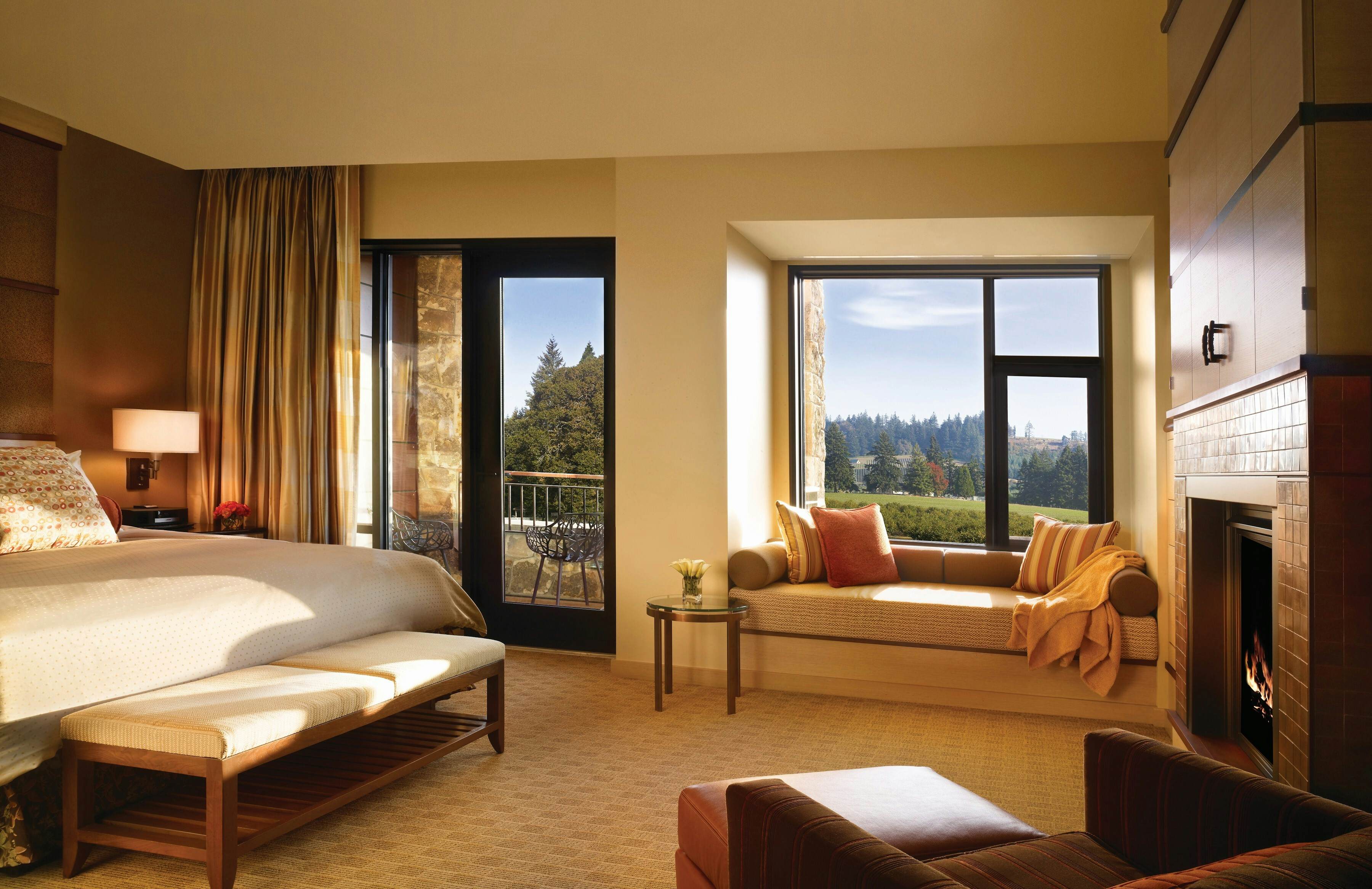 King sized bed with white coverlet with a wall of windows looking out over trees and green space