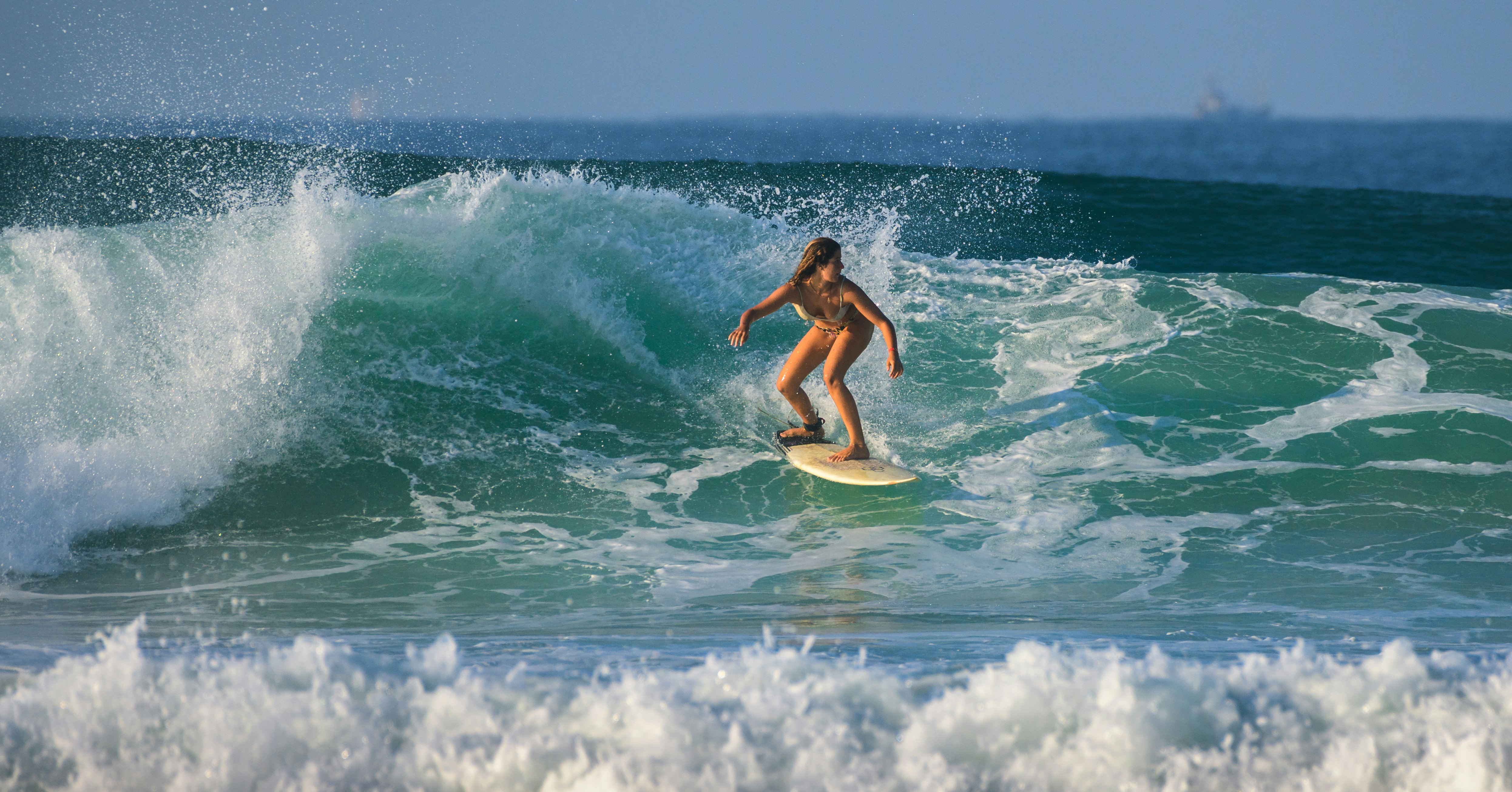 A beautiful talented young surfer girl in a bikini riding a green wave in the morning, Tropical beach vibe.