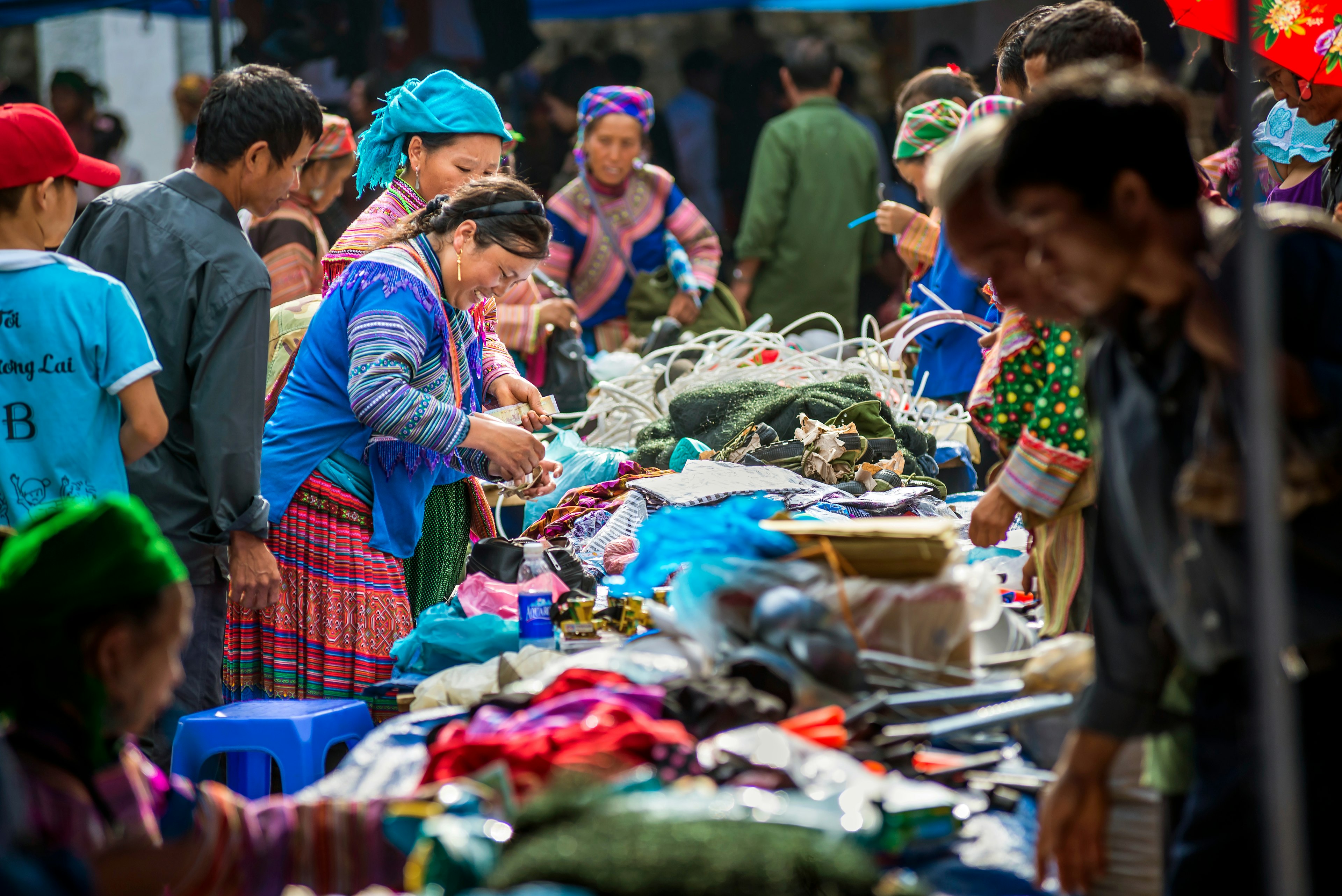 People in colorful, traditional outfits trade dry goods around a table at an outdoor market.