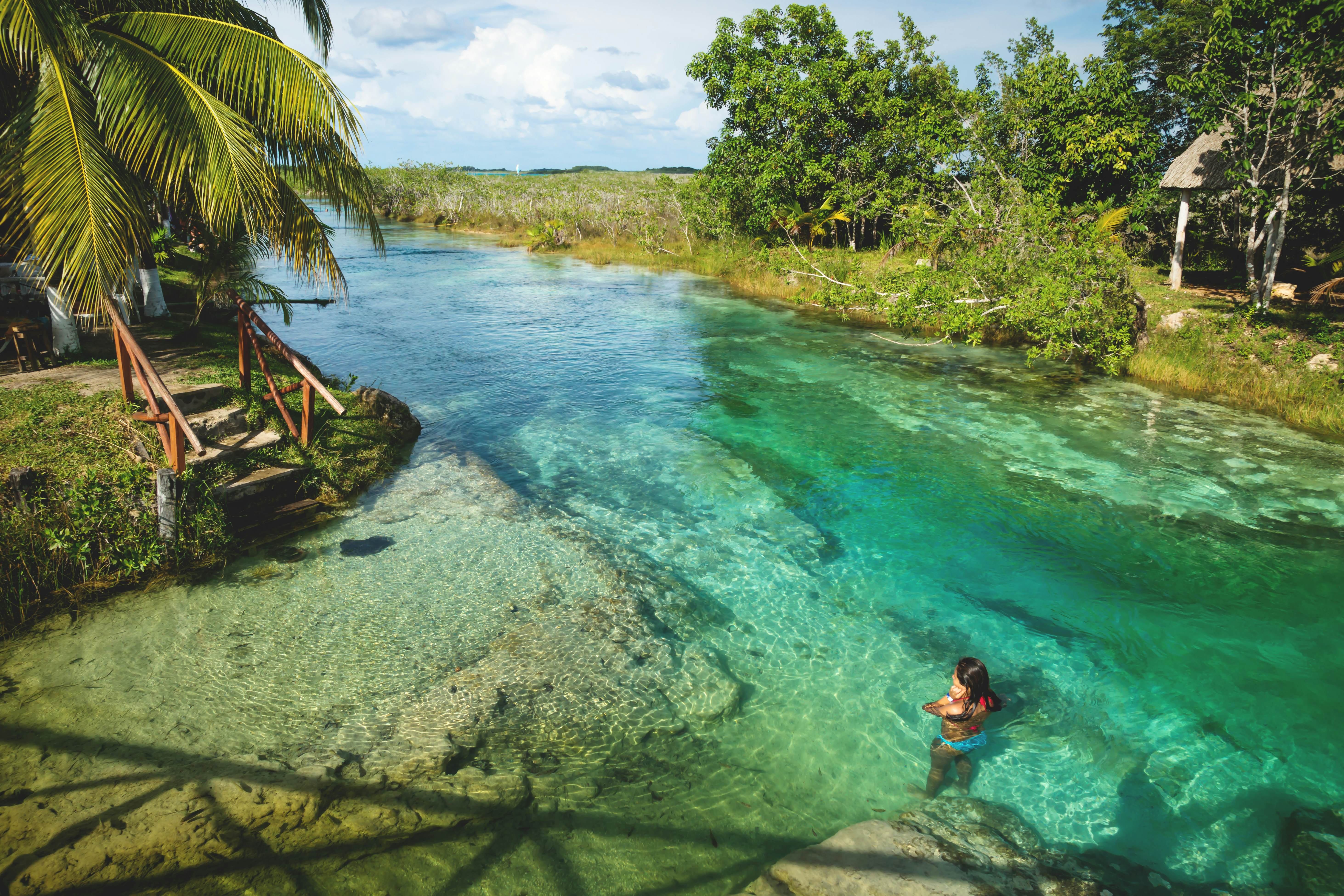 Woman swimming in sunny seven colored lagoon surrounded by tropical plants