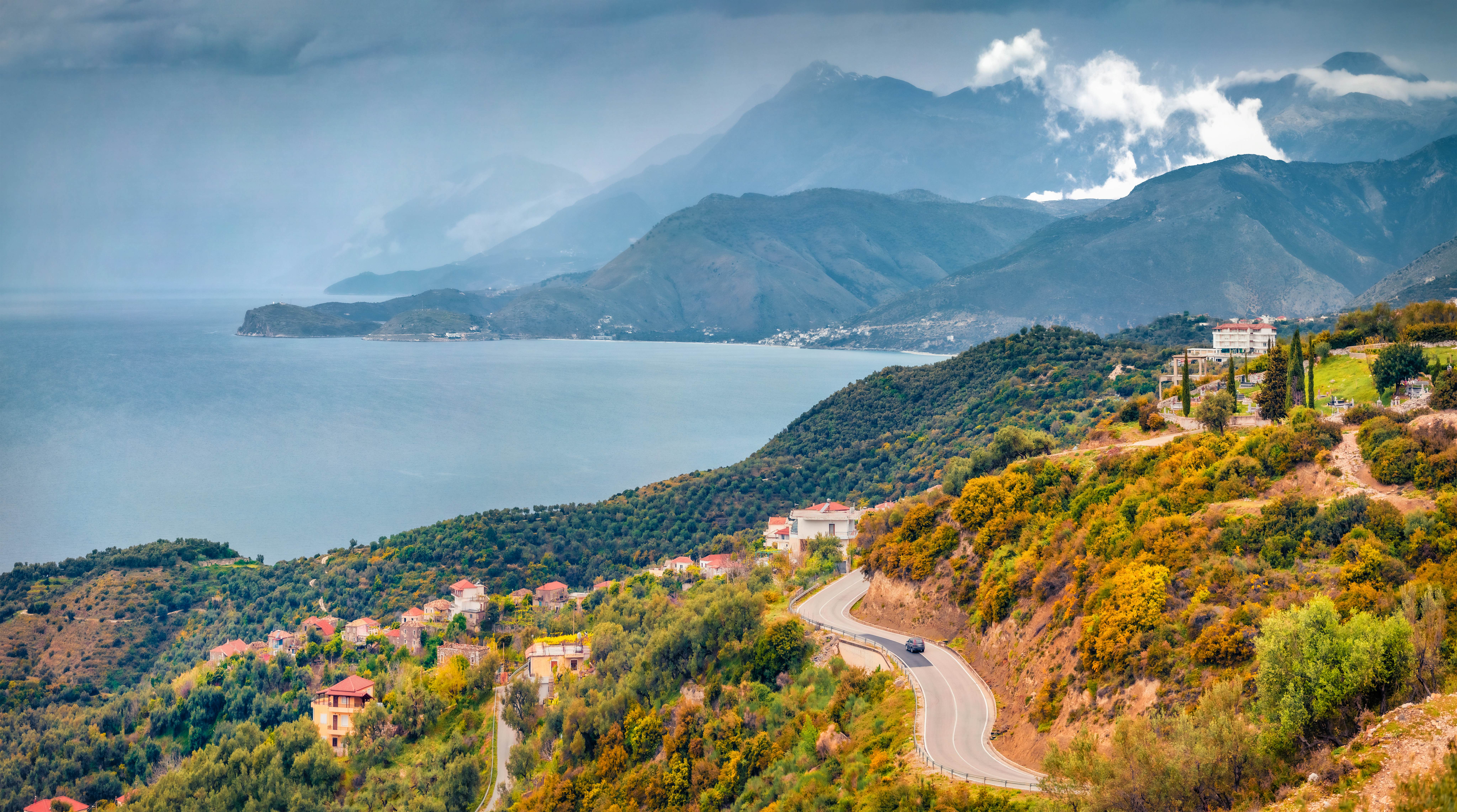 A typical Albanian landscape on the Adriatic shore with asphalt road and misty mountains leading toward the sea.