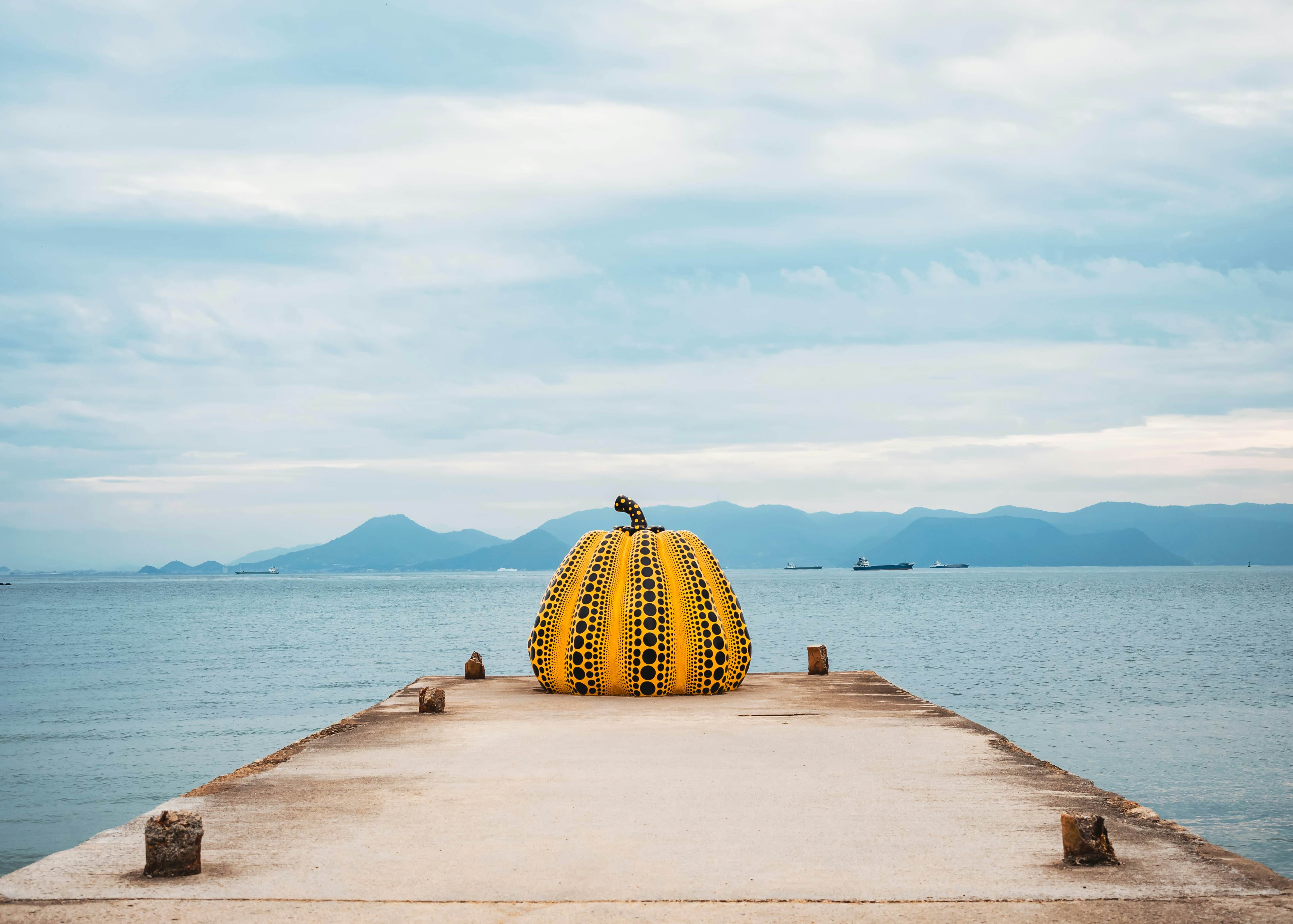 A large art installation of a yellow pumpkin with black spots on the end of a jetty