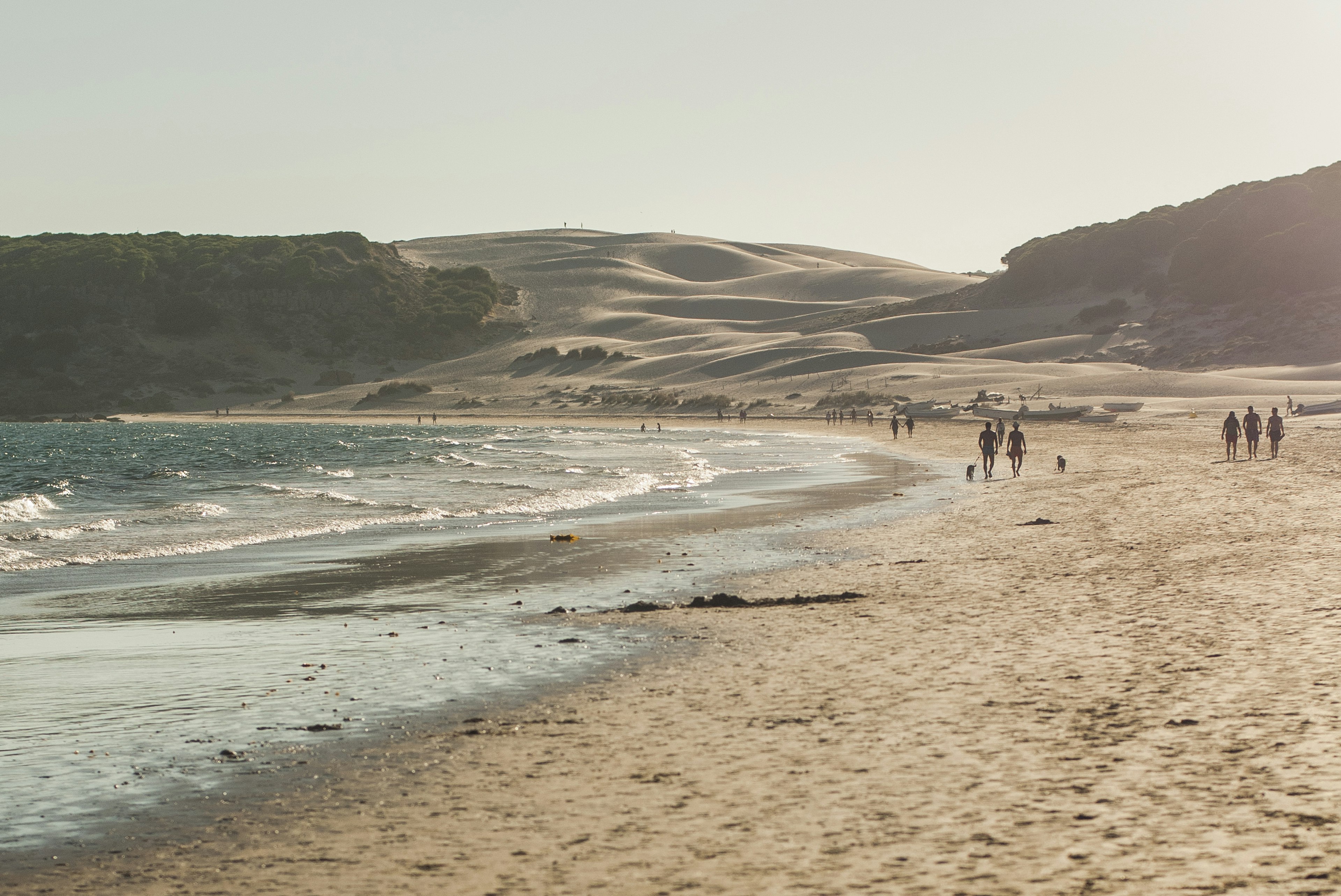 People walk along a golden sand beach backed by sand dunes