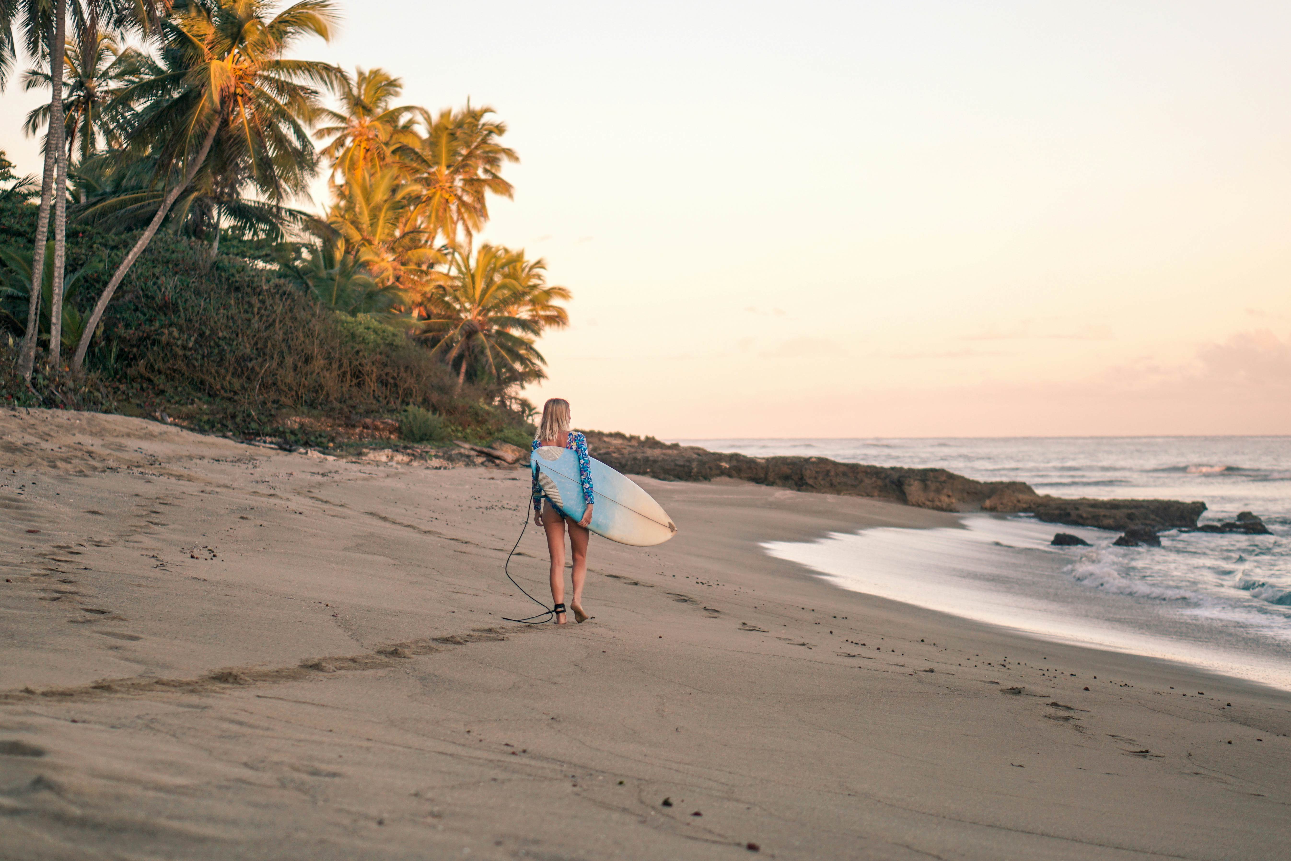 Portrait of blond surfer girl with white surf board in blue ocean pictured from the water in Encuentro beach in Dominican Republic.