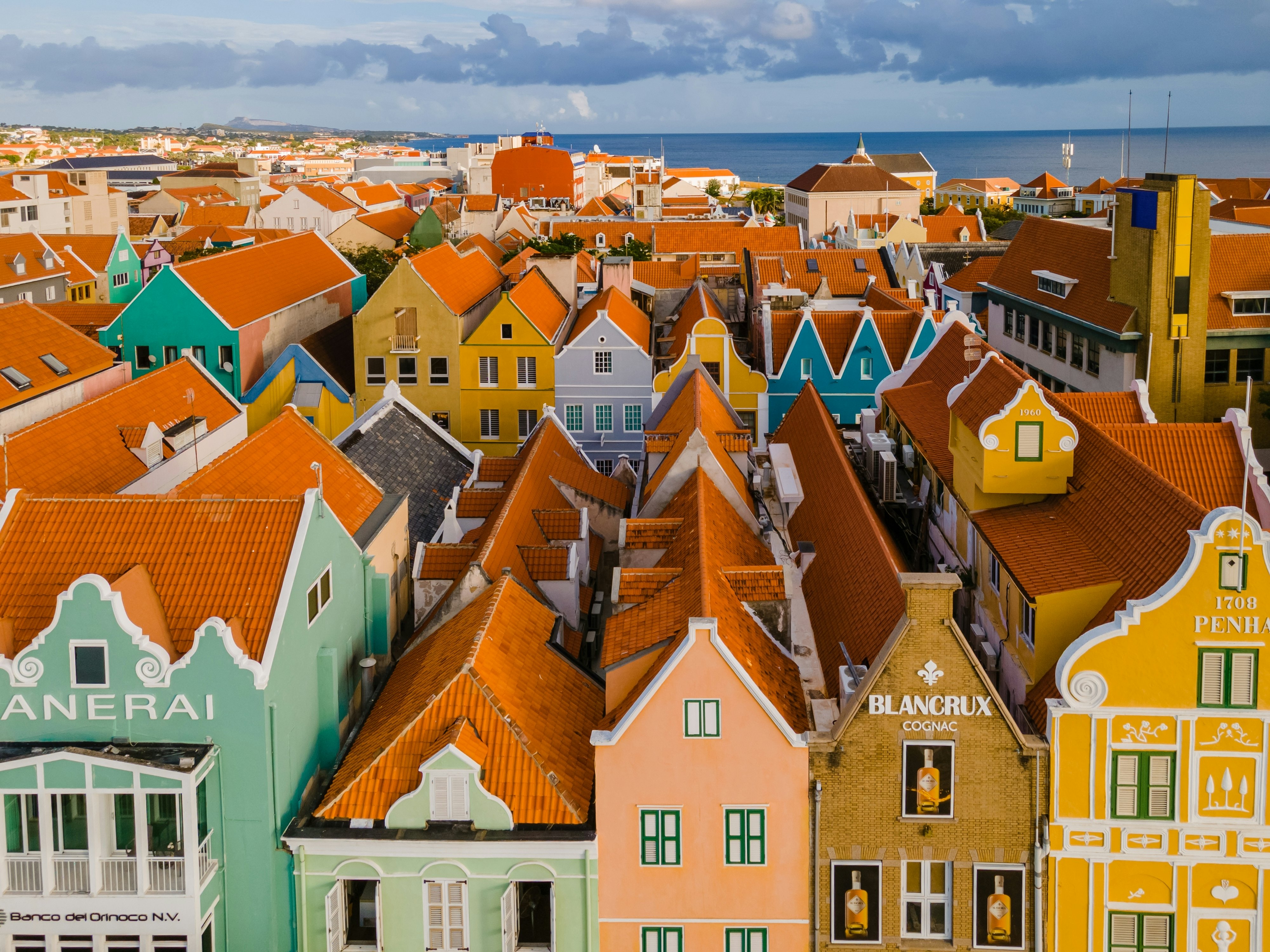 An aerial view of red-tiled roofs of buildings with facades painted in pastel colors in a tropical city.