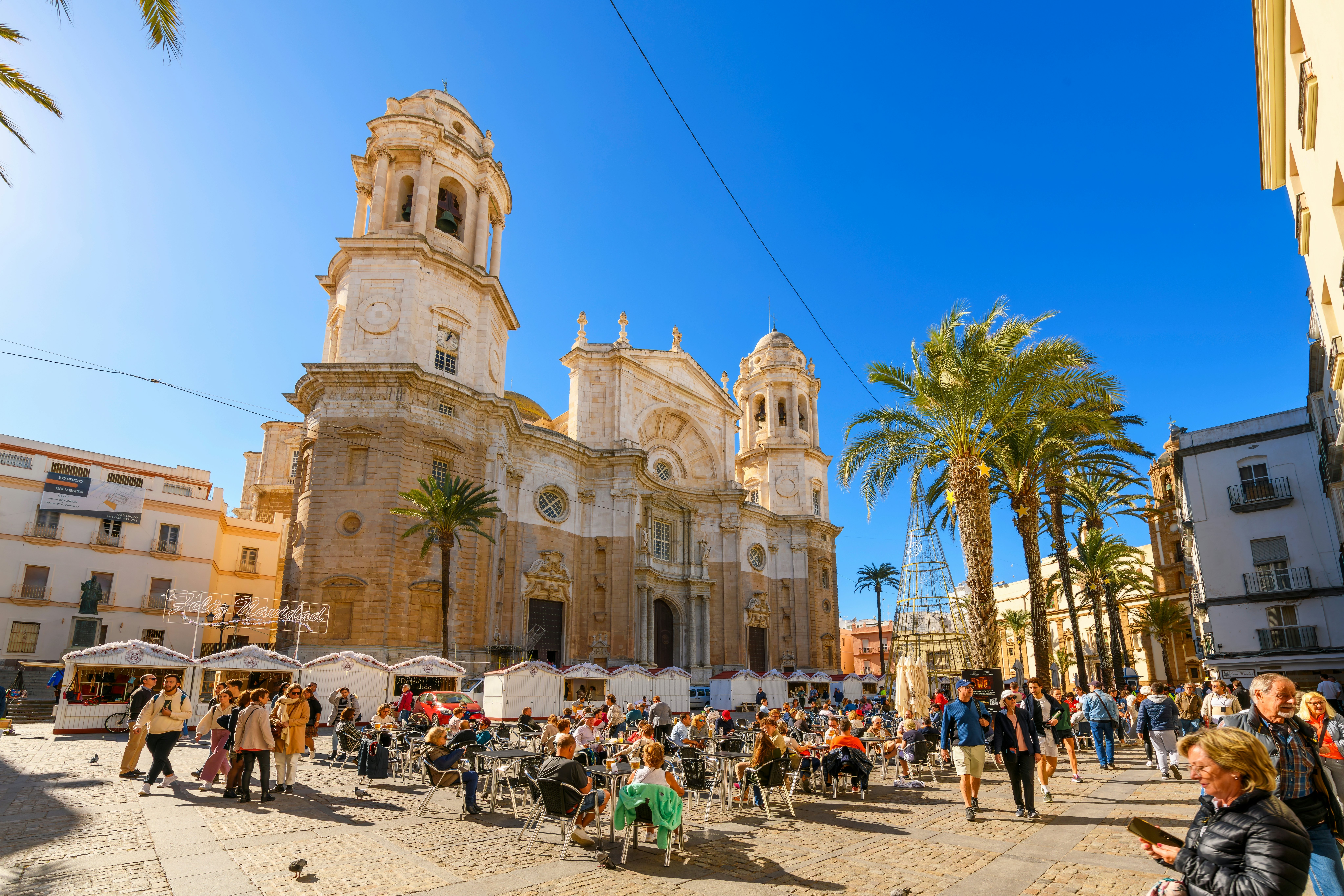 Tourists dine in the sun at in a square near a cathedral