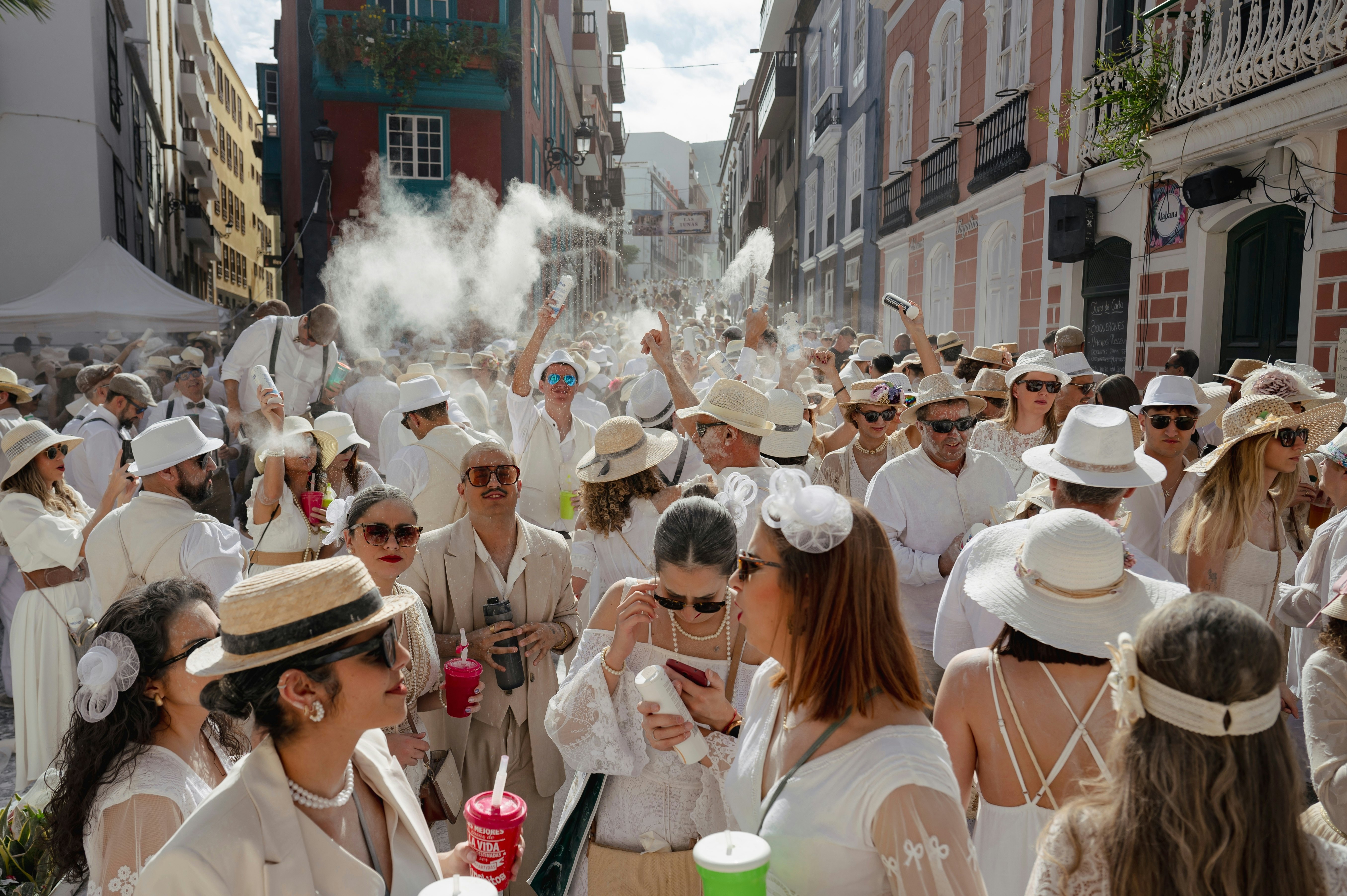 People dressed in festive white costumes toss talcum powder at one another during a street party in a city.