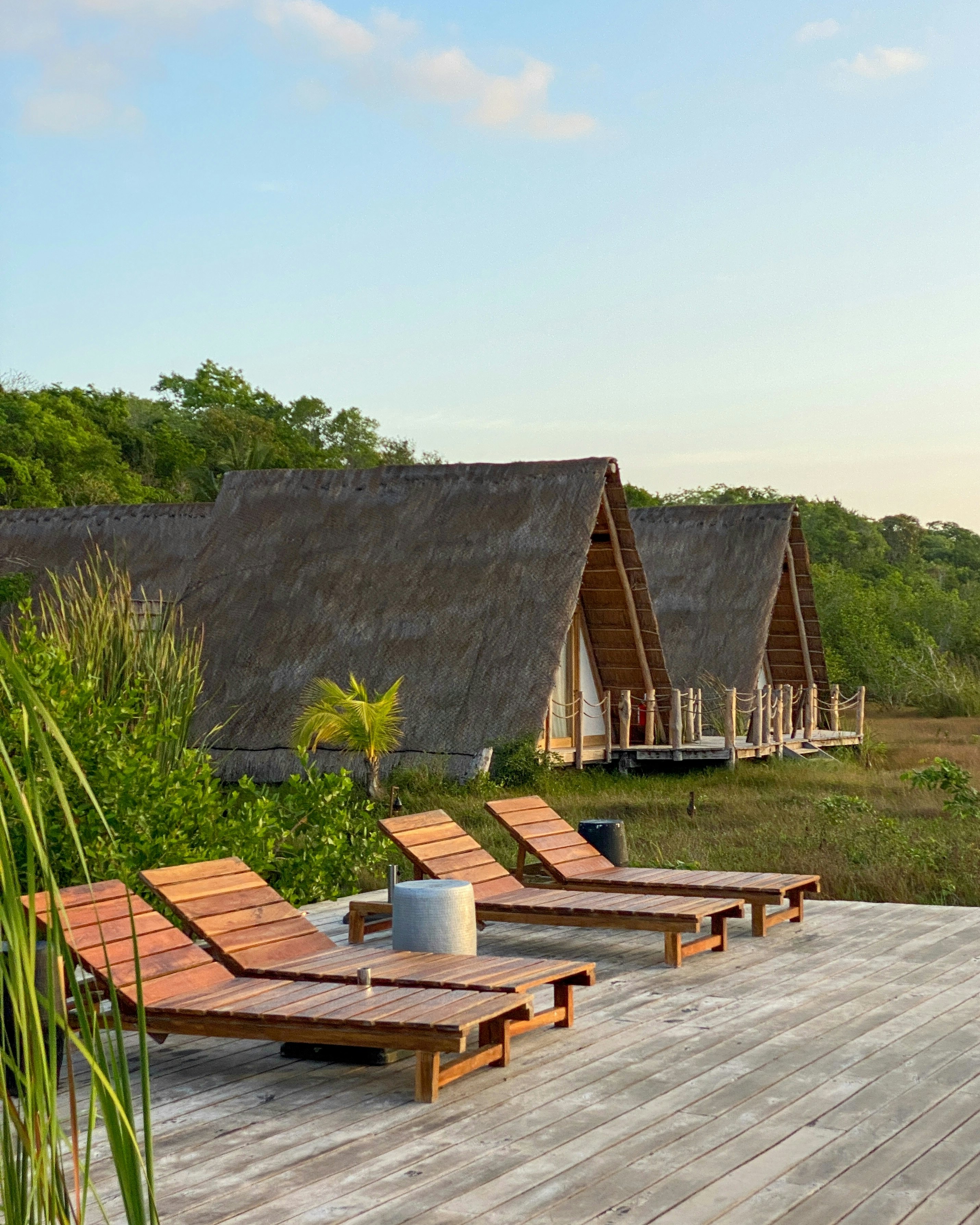 Terrace with sun loungers and in the background wooden cabins of the luxury jungle hotel