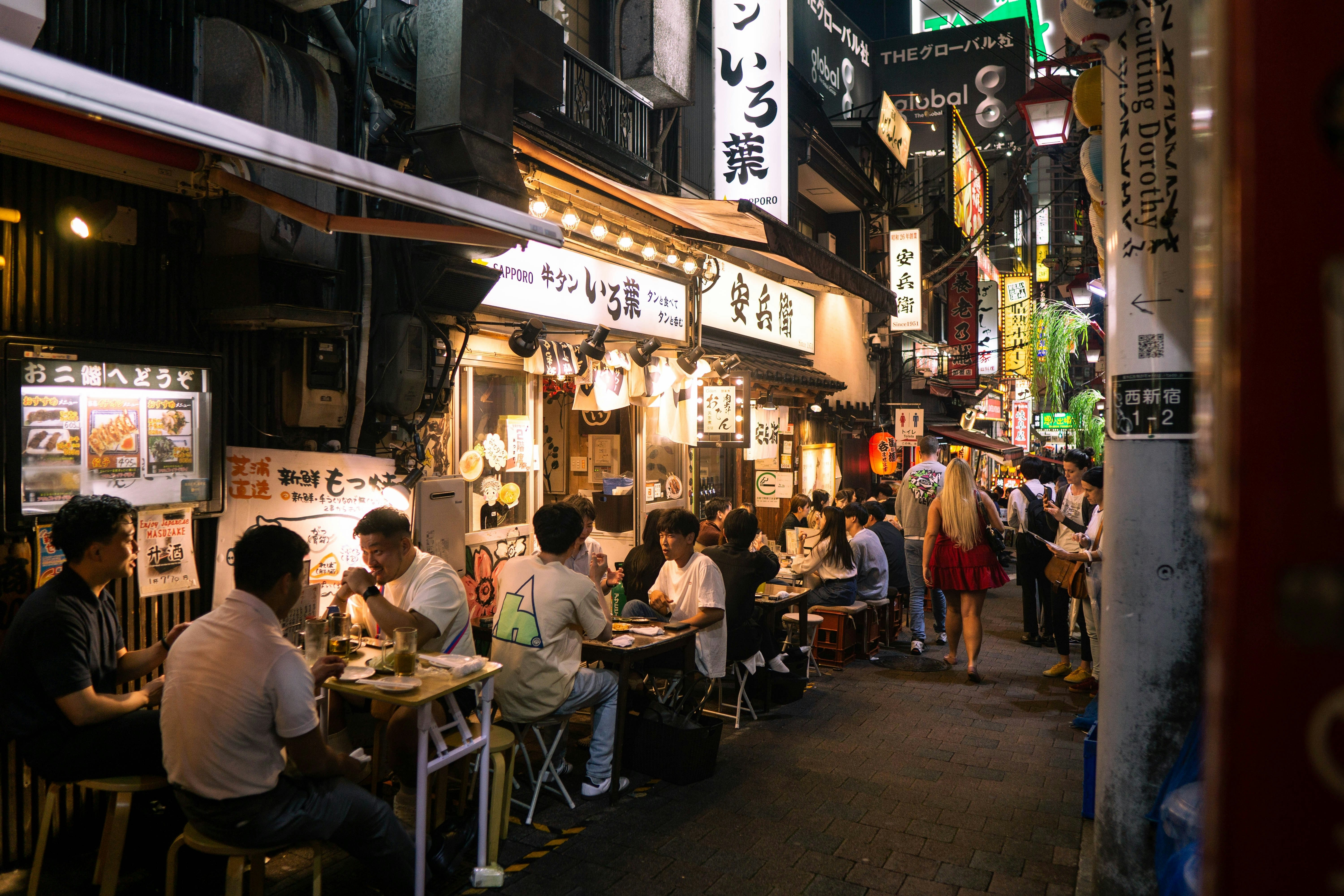 Tourists and locals enjoying drinks and skewers in a small alley. The vibrant izakaya bars in Omoide Yokocho capture the essence of Japan's night life.