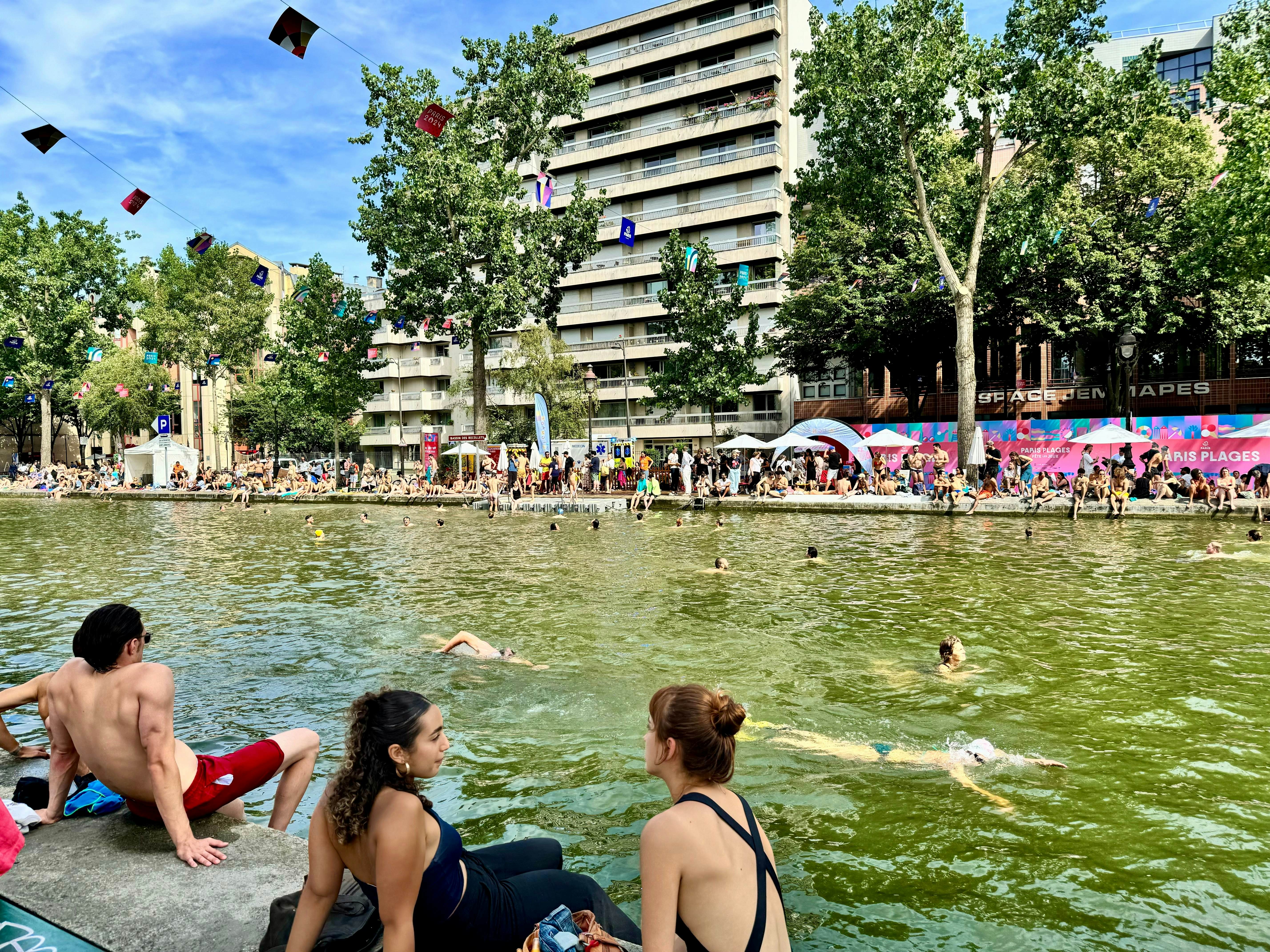 Two young women in bathing suits sunbathing and talking at the open Bassin des Recollets at Canal Saint-Martin in Paris, France