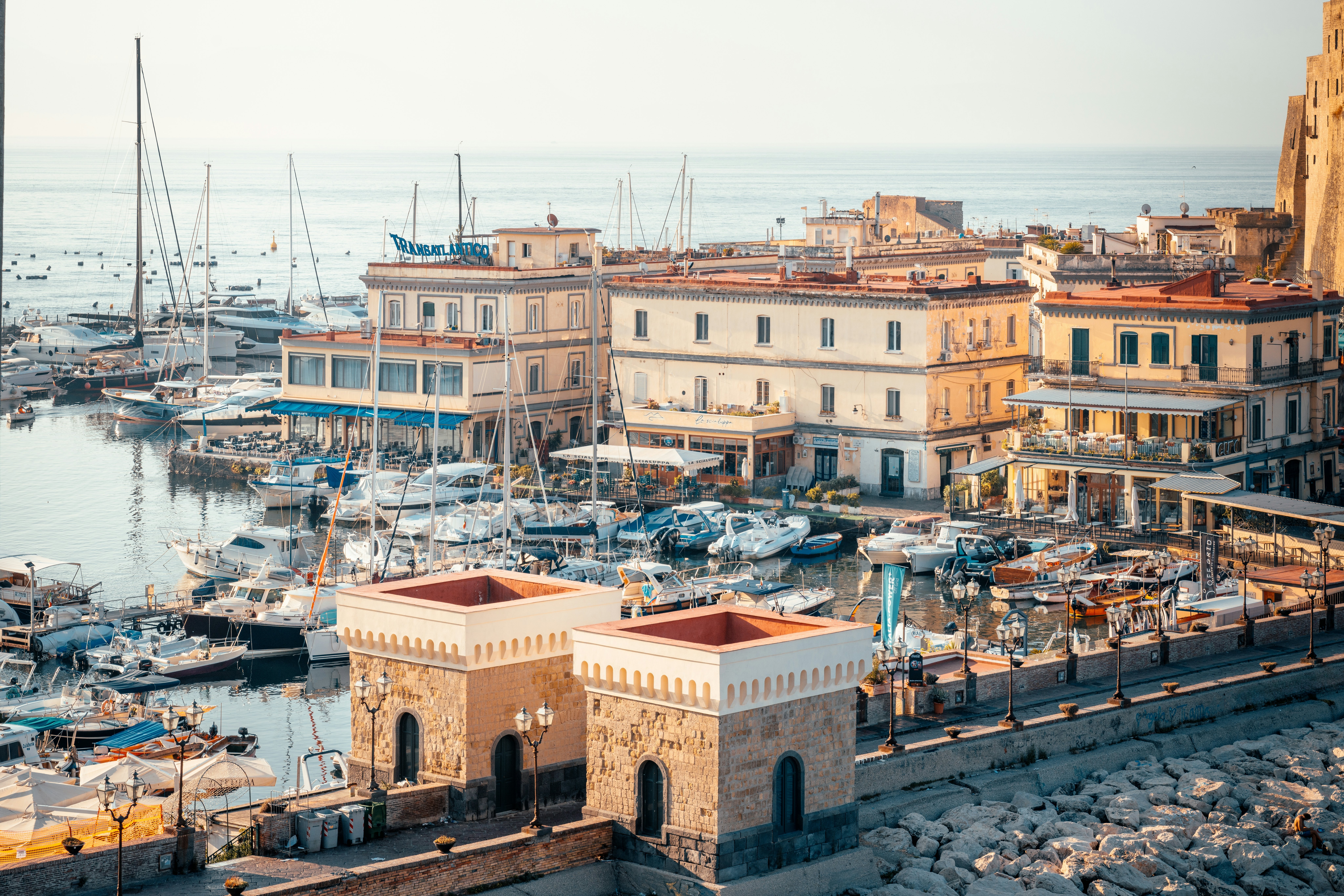 A tightly packed city harbor with many yachts and small boats docked in the sunshine.