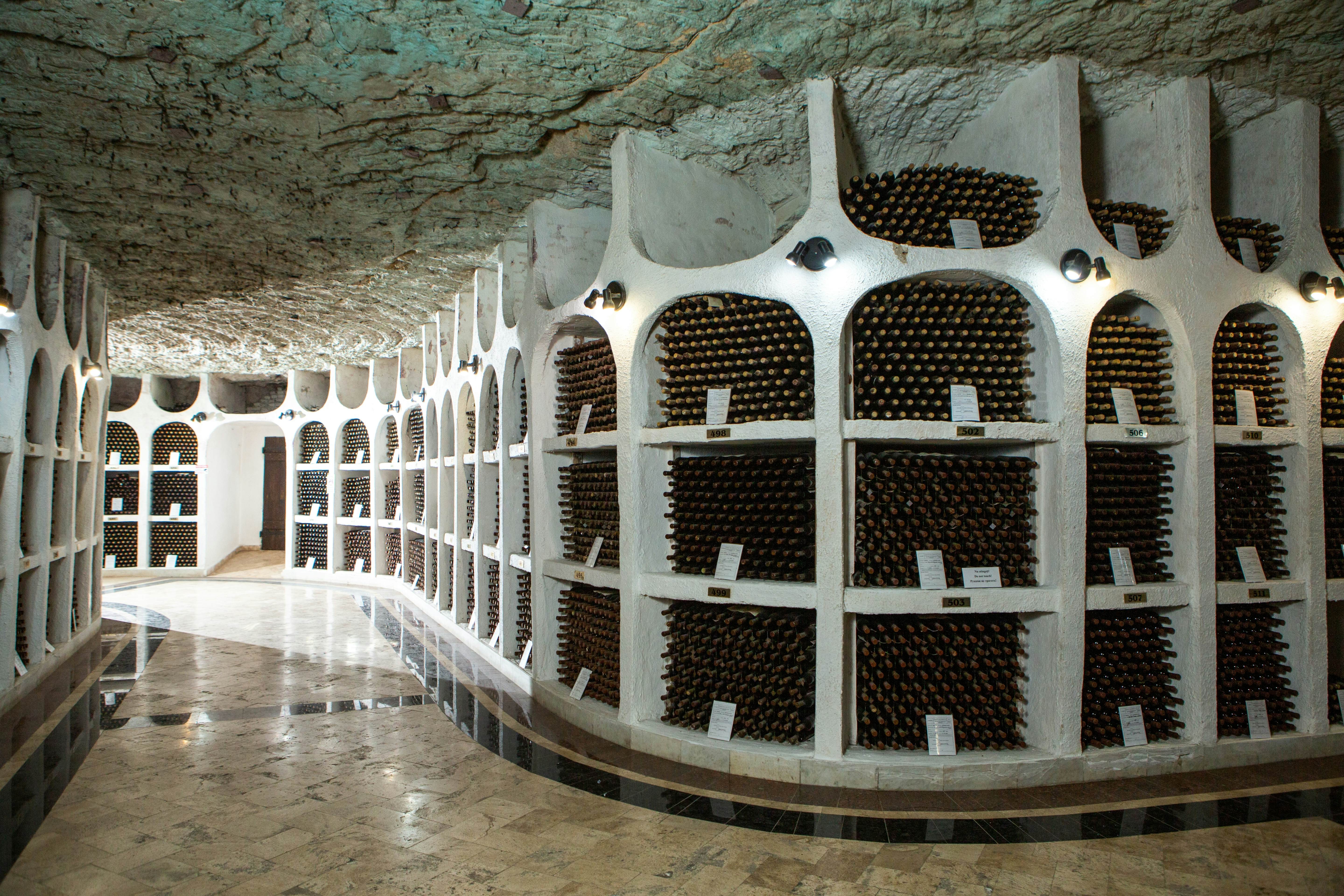 A wall of arched cubbies holes filled with wine bottles in a vast cellar