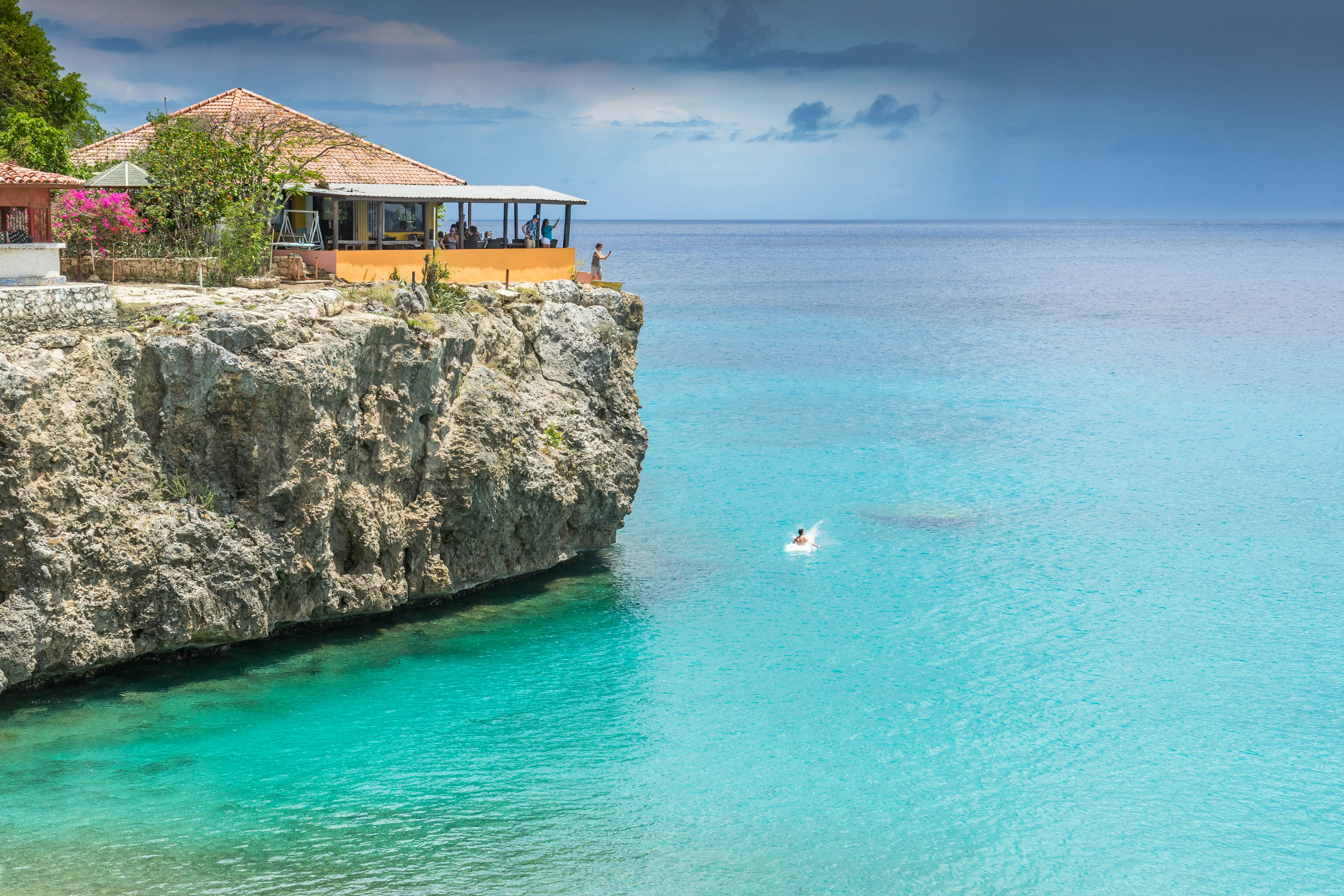 A person in the ocean below a platform on the cliff that they've just jumped from