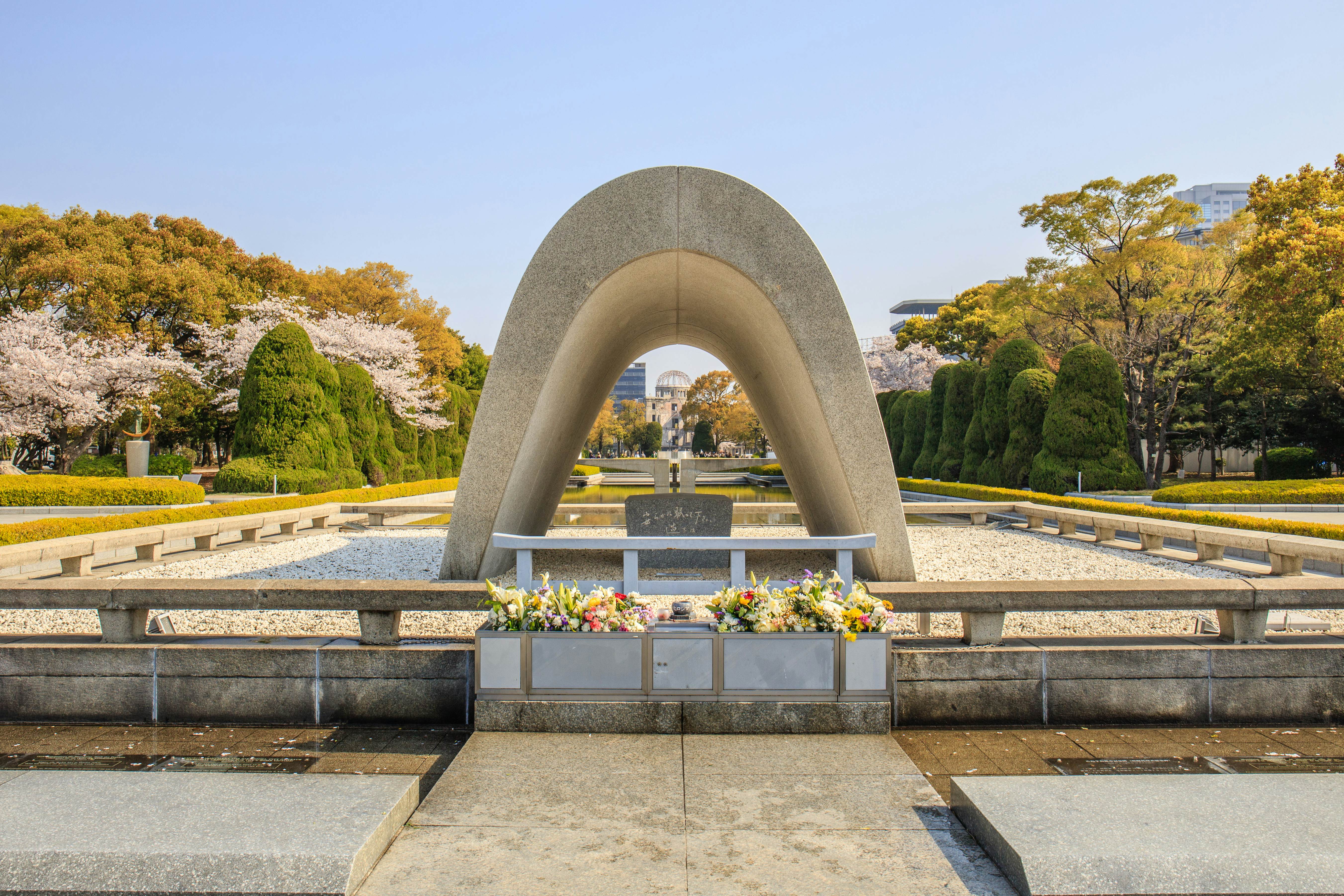 An arched memorial with flowers in front. Through the arch in the distance is a building with a damaged dome