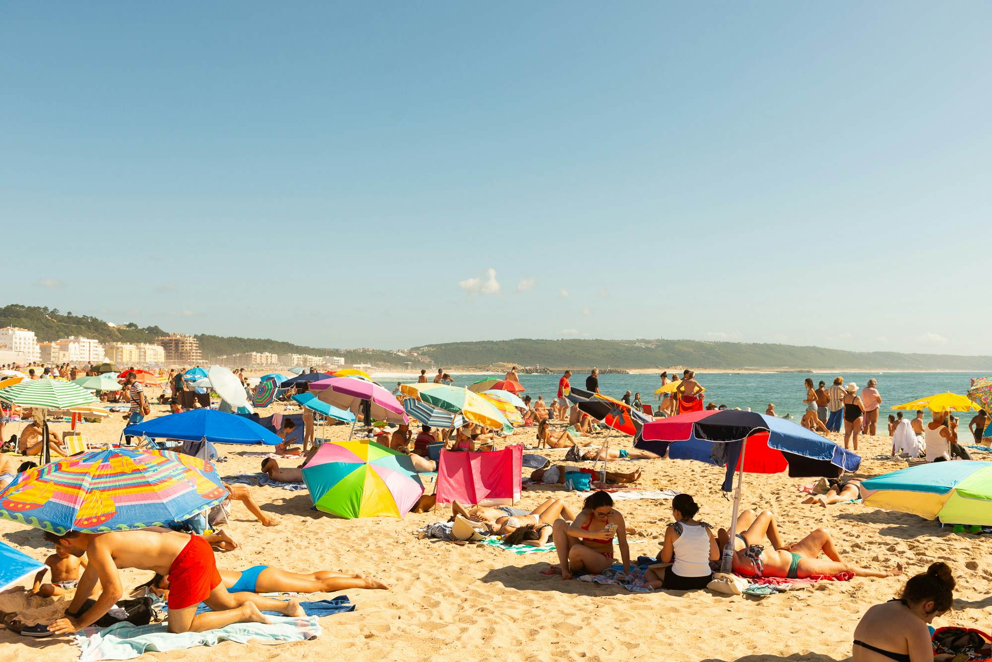 Umbrellas and sunbathers on the beach in Nazaré, Portugal