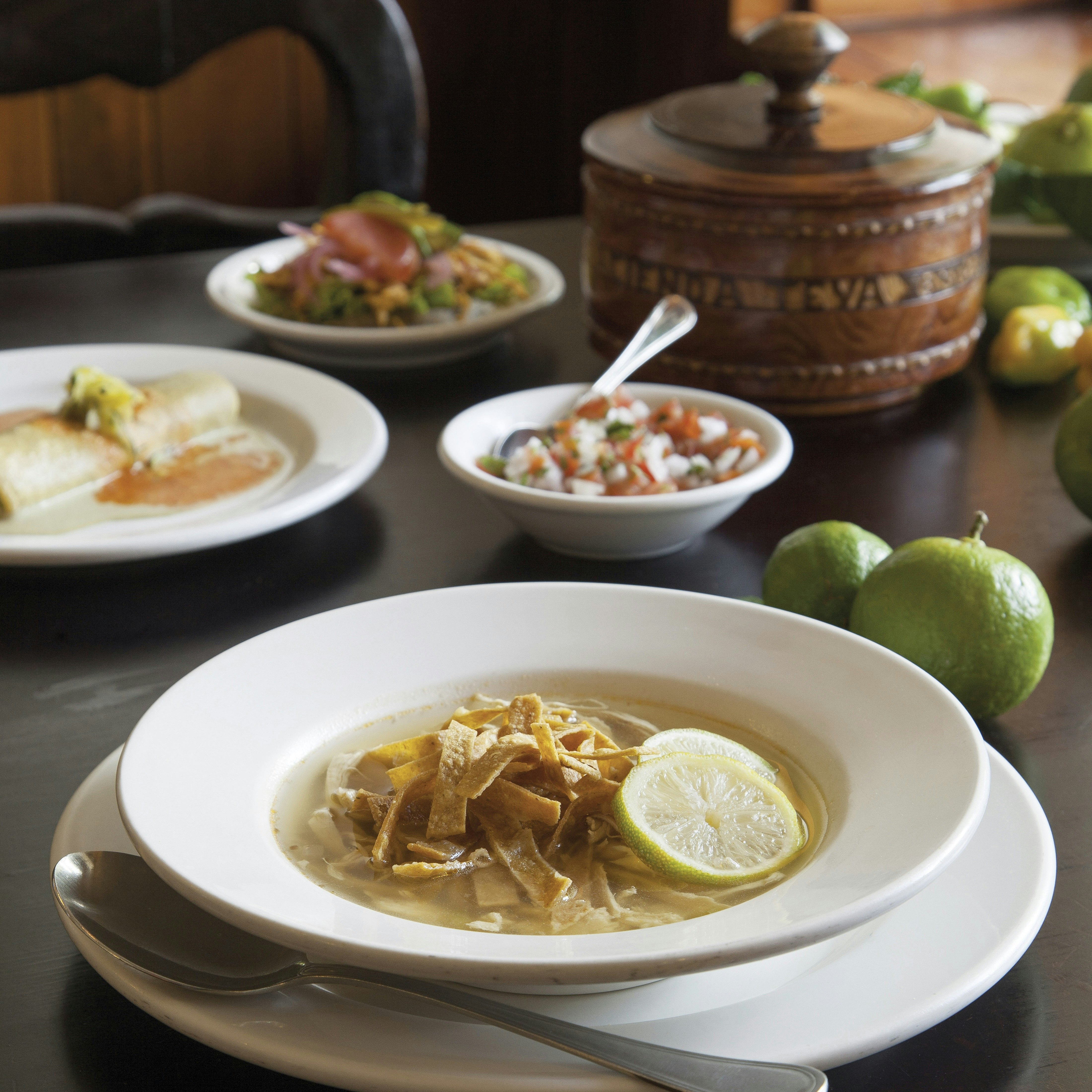 A series of dishes, including a soup, pico de gallo and several limes, sit on a table at a restaurant in Mexico.