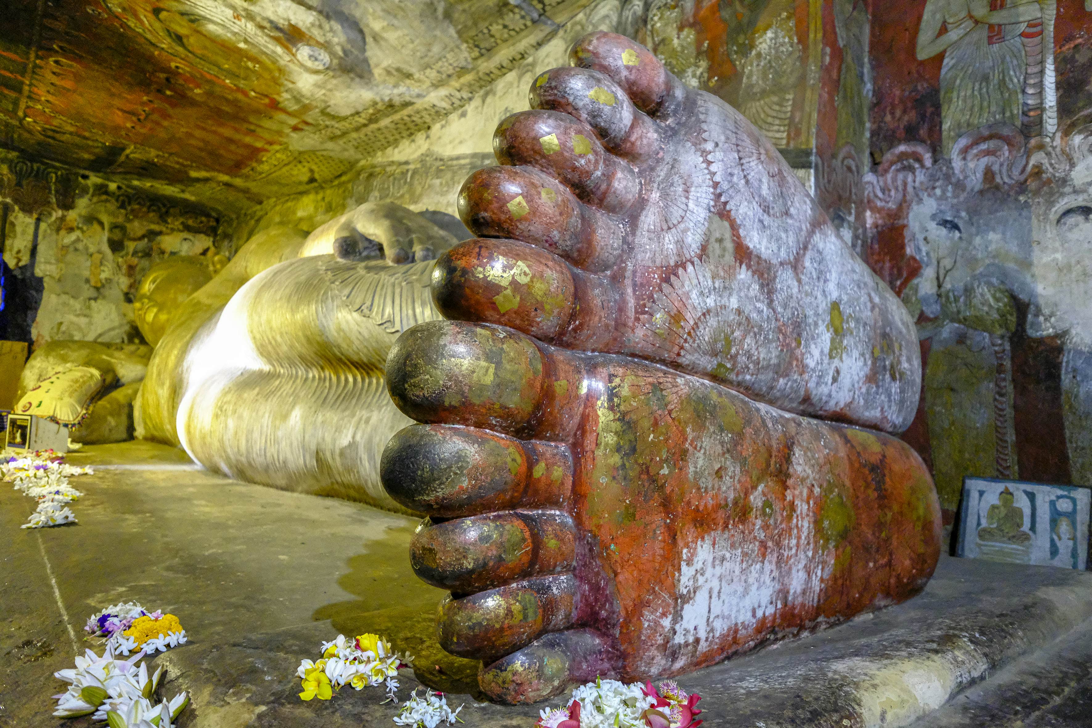 A large reclining Buddha statue in a cave with murals painted on the feet and surrounding walls