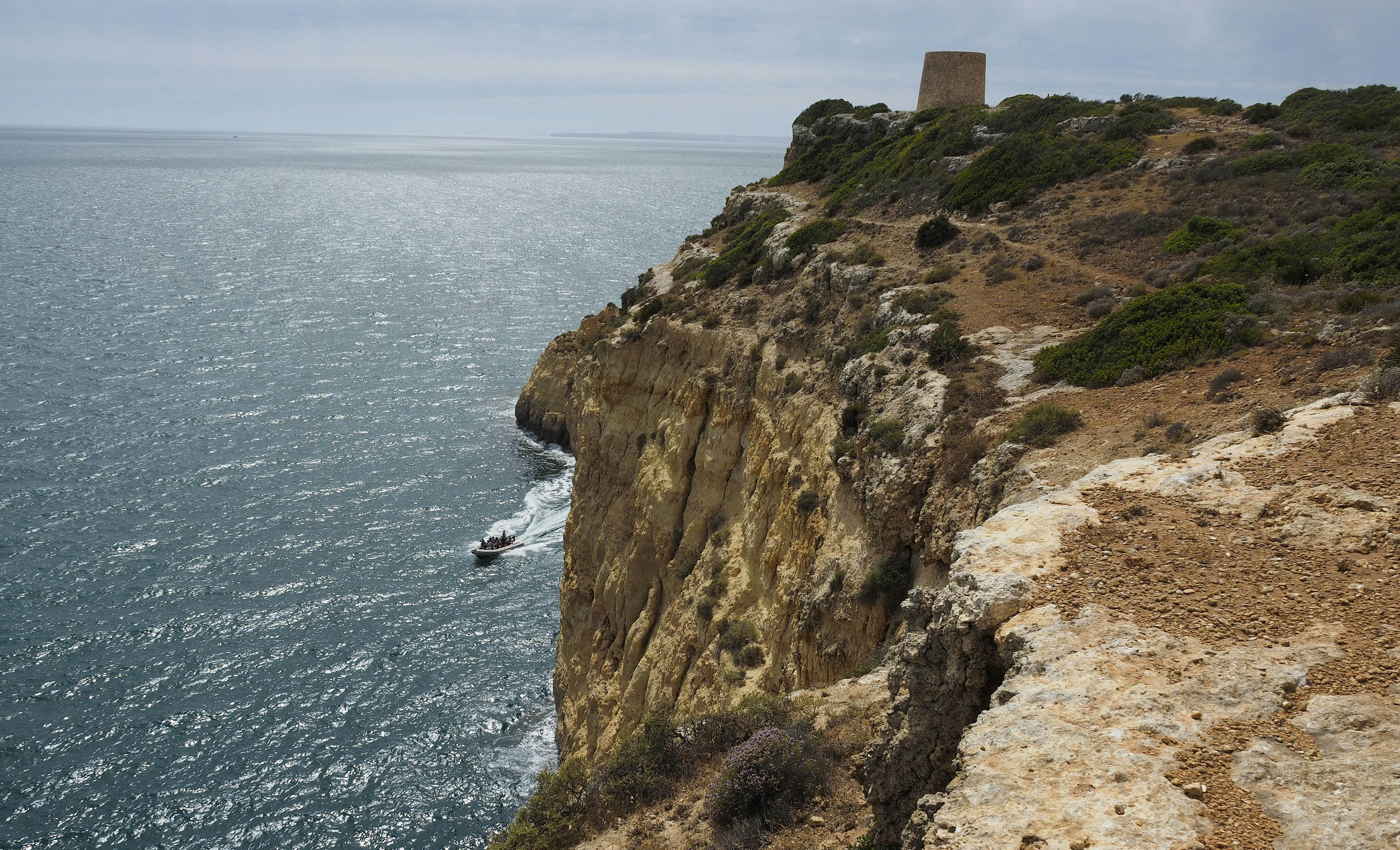 A rocky cliff top towering over the sea, leading to a stout stone lookout tower