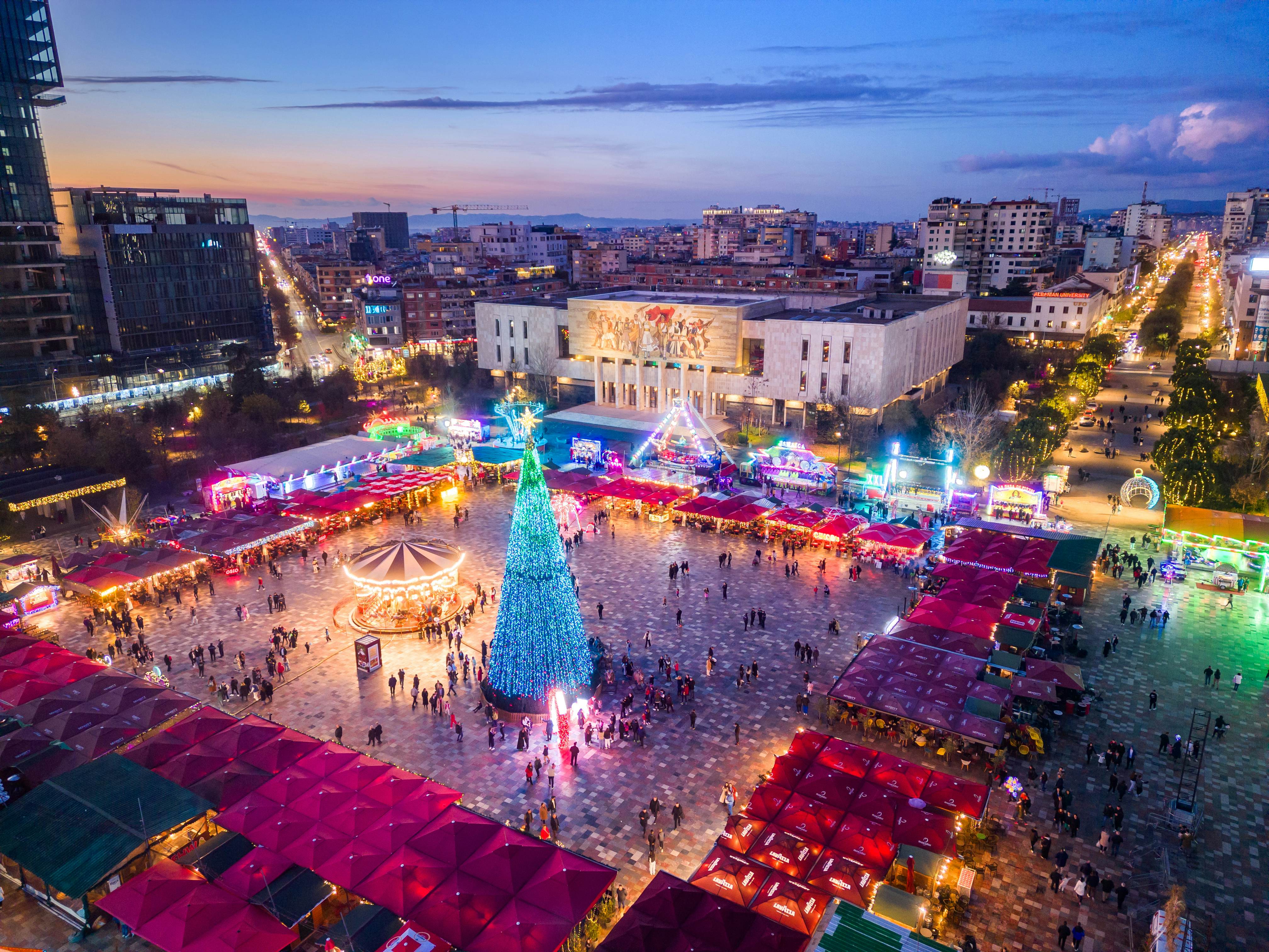 A city square lined with stalls and lit up in neon lights at dusk