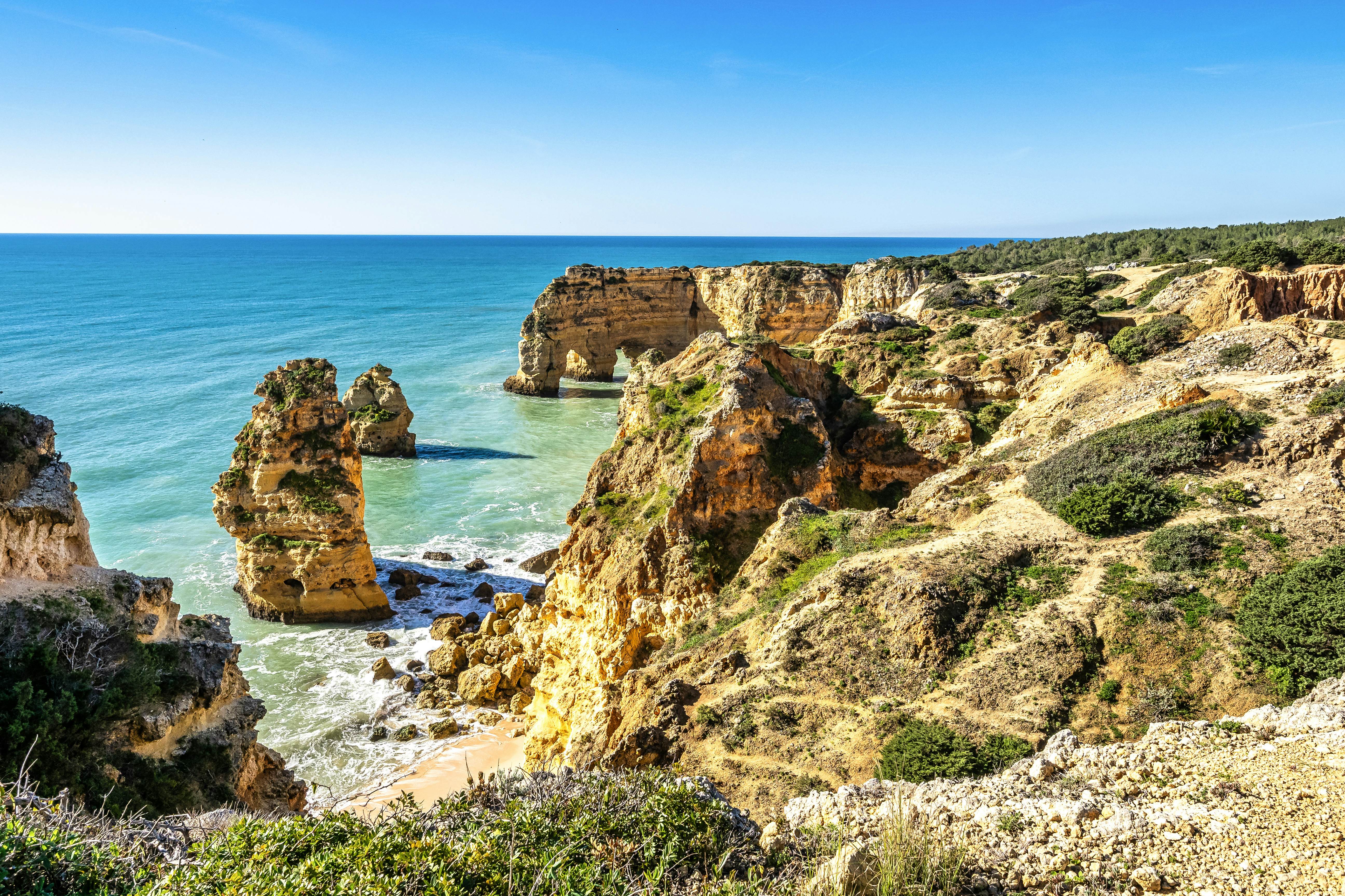 Rocky stacks and archways out to sea with a tiny sandy cove at the foot of the cliff