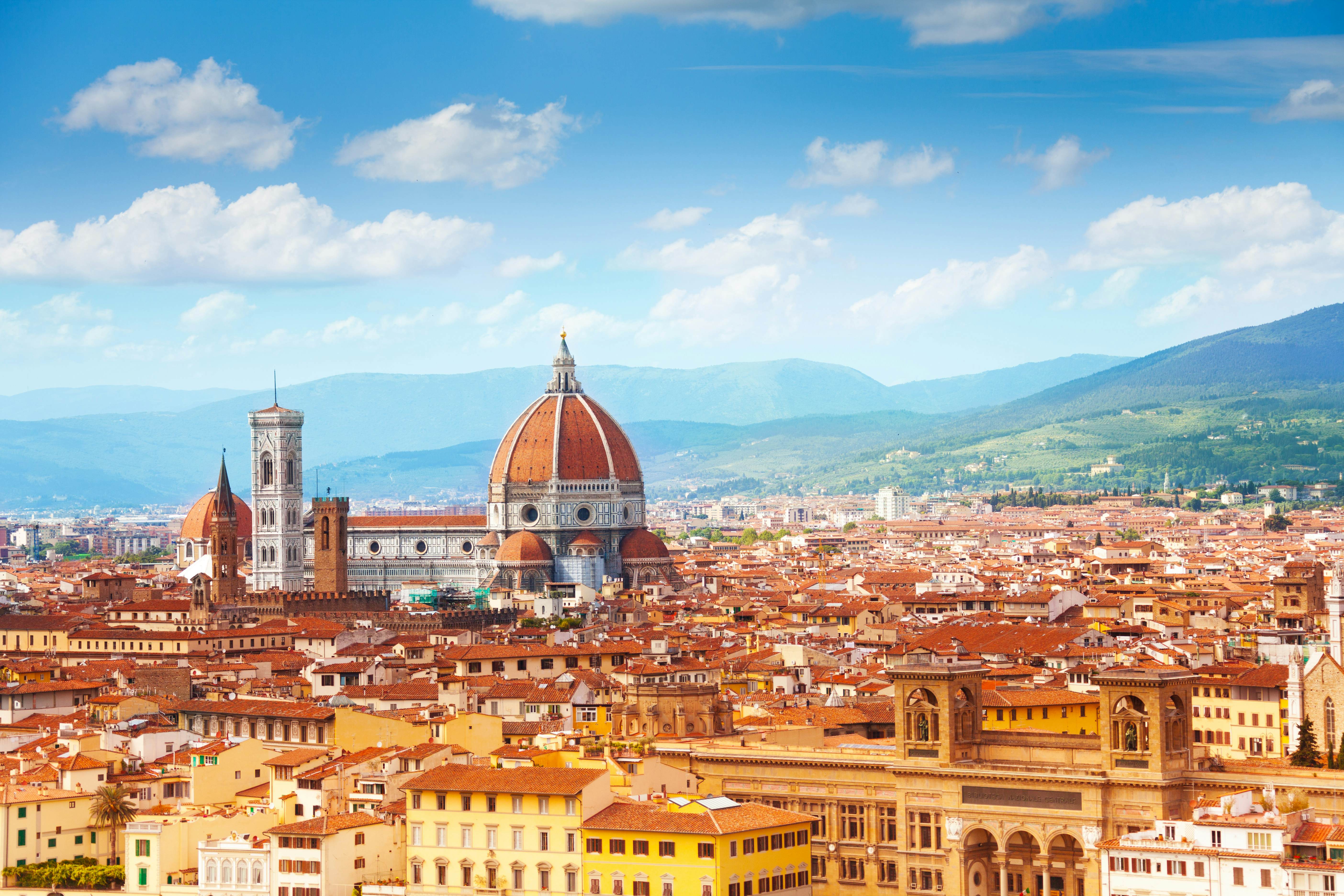 A cityskyline with a central domed cathedral surrounded by low-rise red-roofed buildings