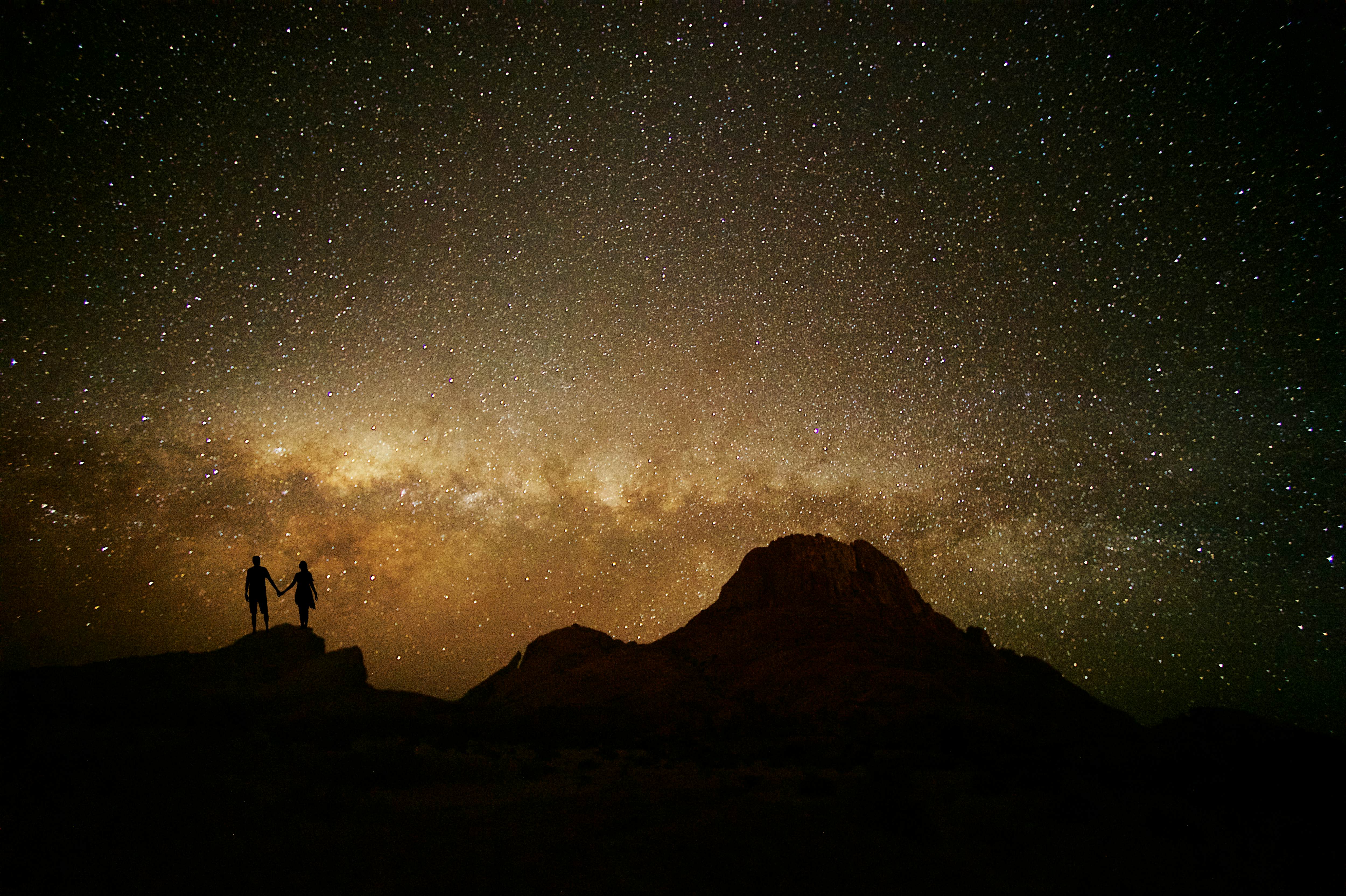 Silhouette of the back of a young male and female couple standing on a rock facing towards a spectacular star Milky Way Mountain Namibian Desert Spitzkoppe Namibia Africa