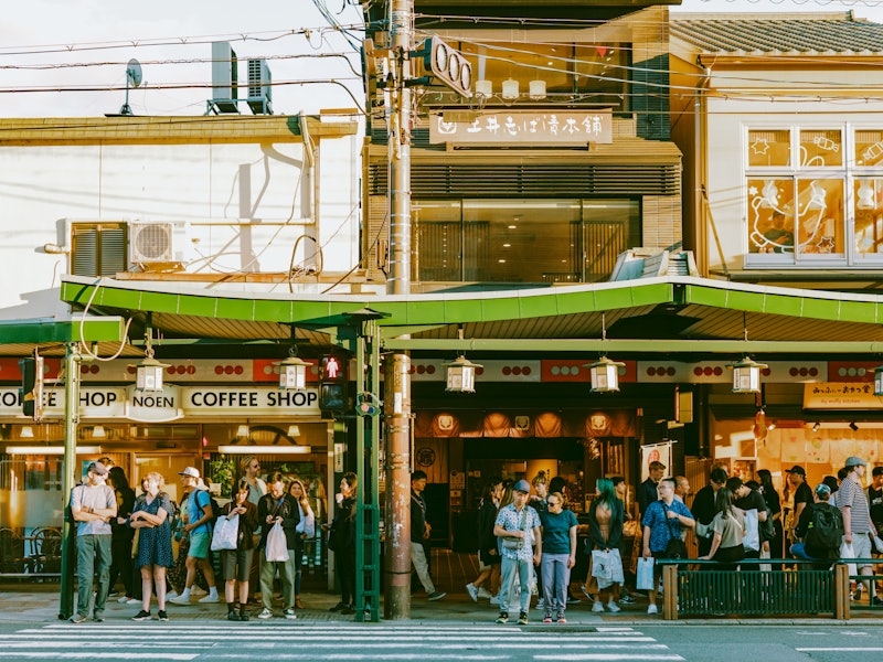 People wait to cross the street in front of a busy cafe