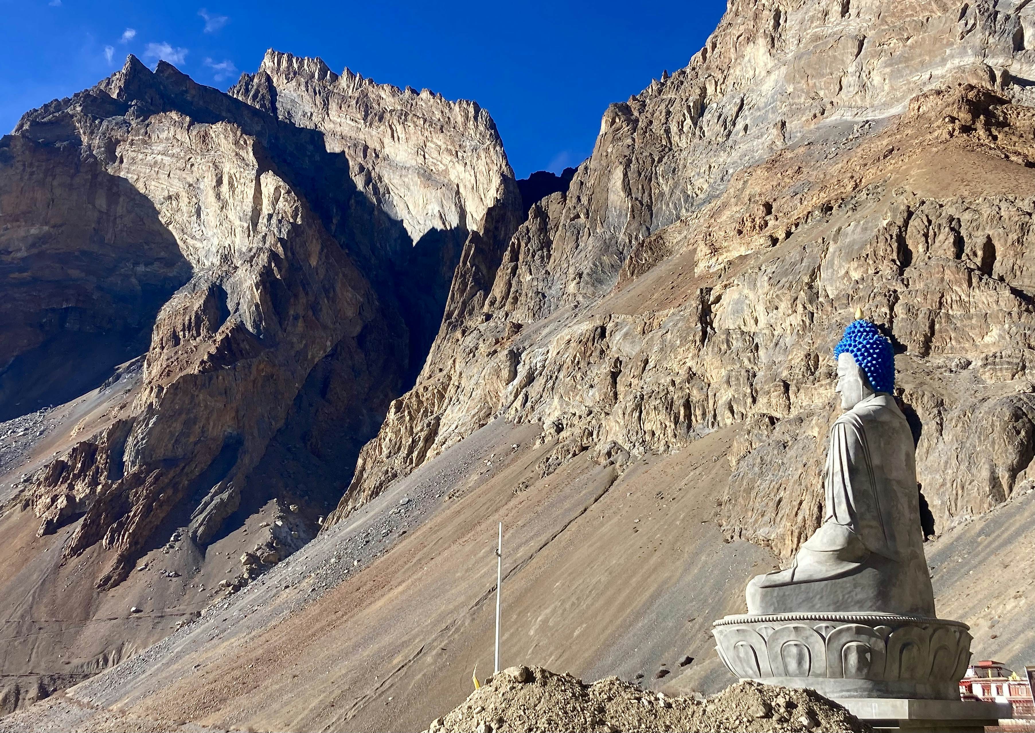 A large Buddha statue sits facing the valley with rugged sandstone mountains in the background.