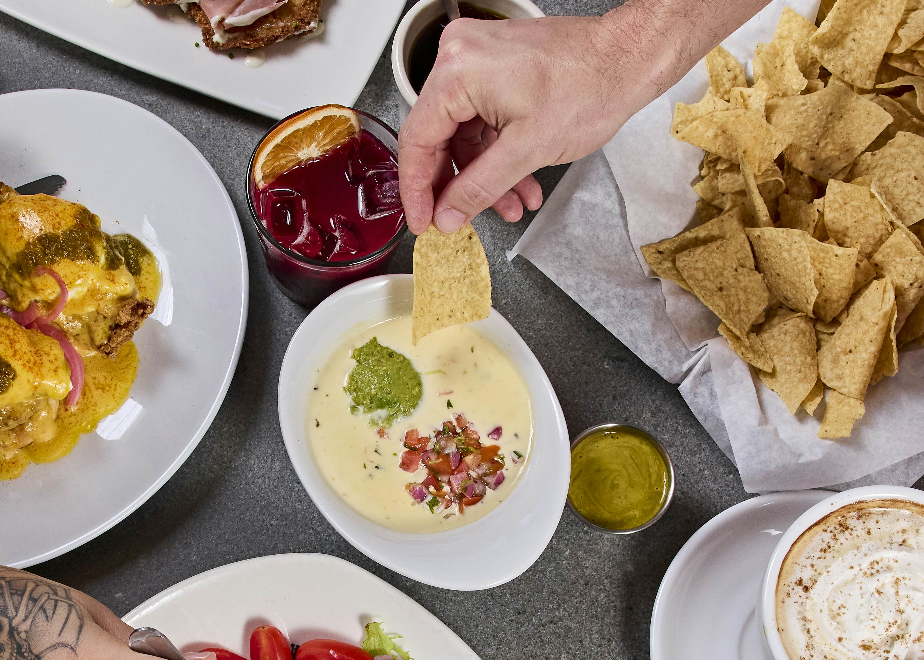 Order of food with queso in the middle. A bowl of chips, a red drink with ice and a queso covered giant burrito