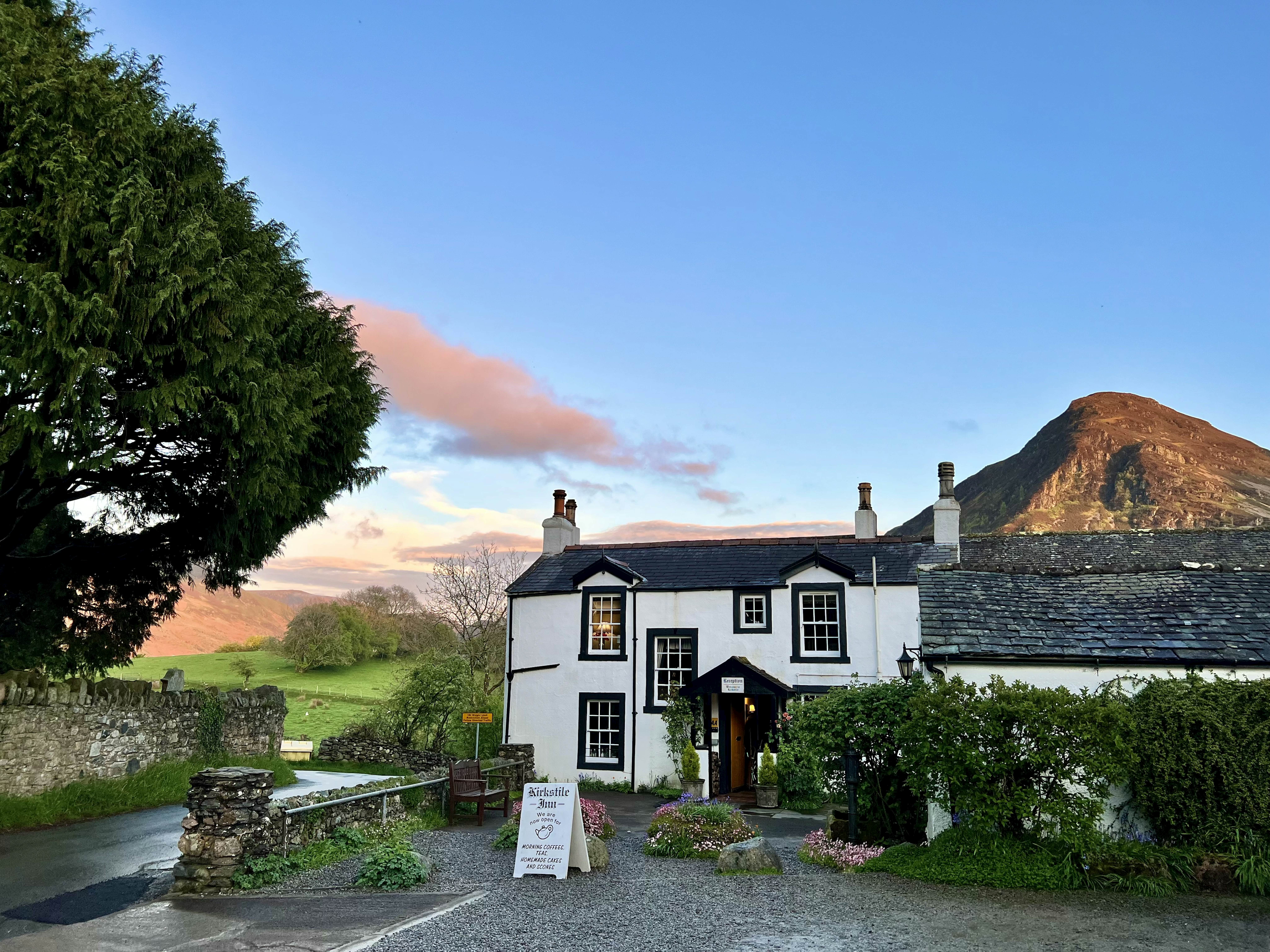 Exterior of the Kirkstile Inn and pub in England's Lake District, with the sun setting over the hills in the background