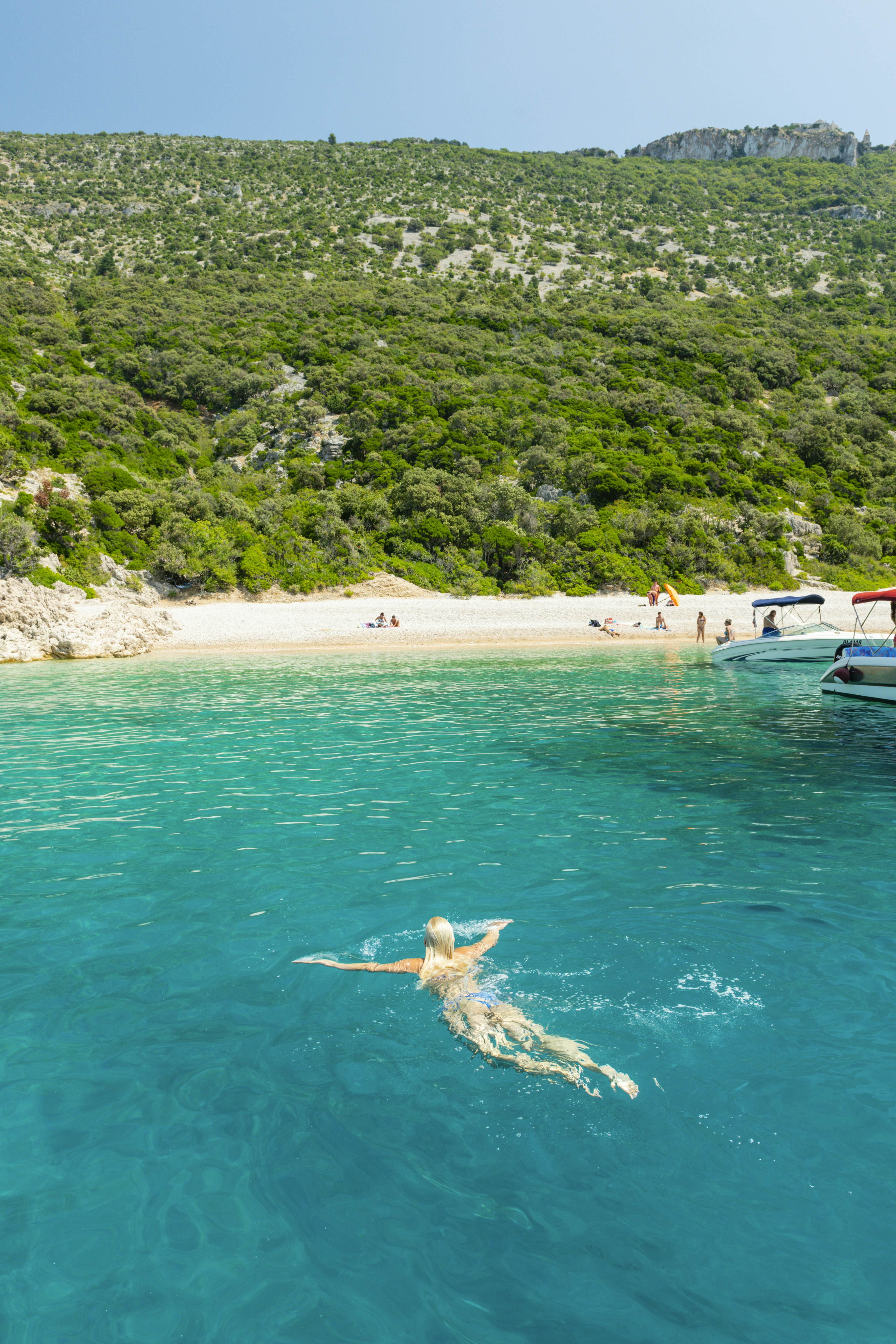 A woman swims through turquoise water near a beach backed by dense undergrowth