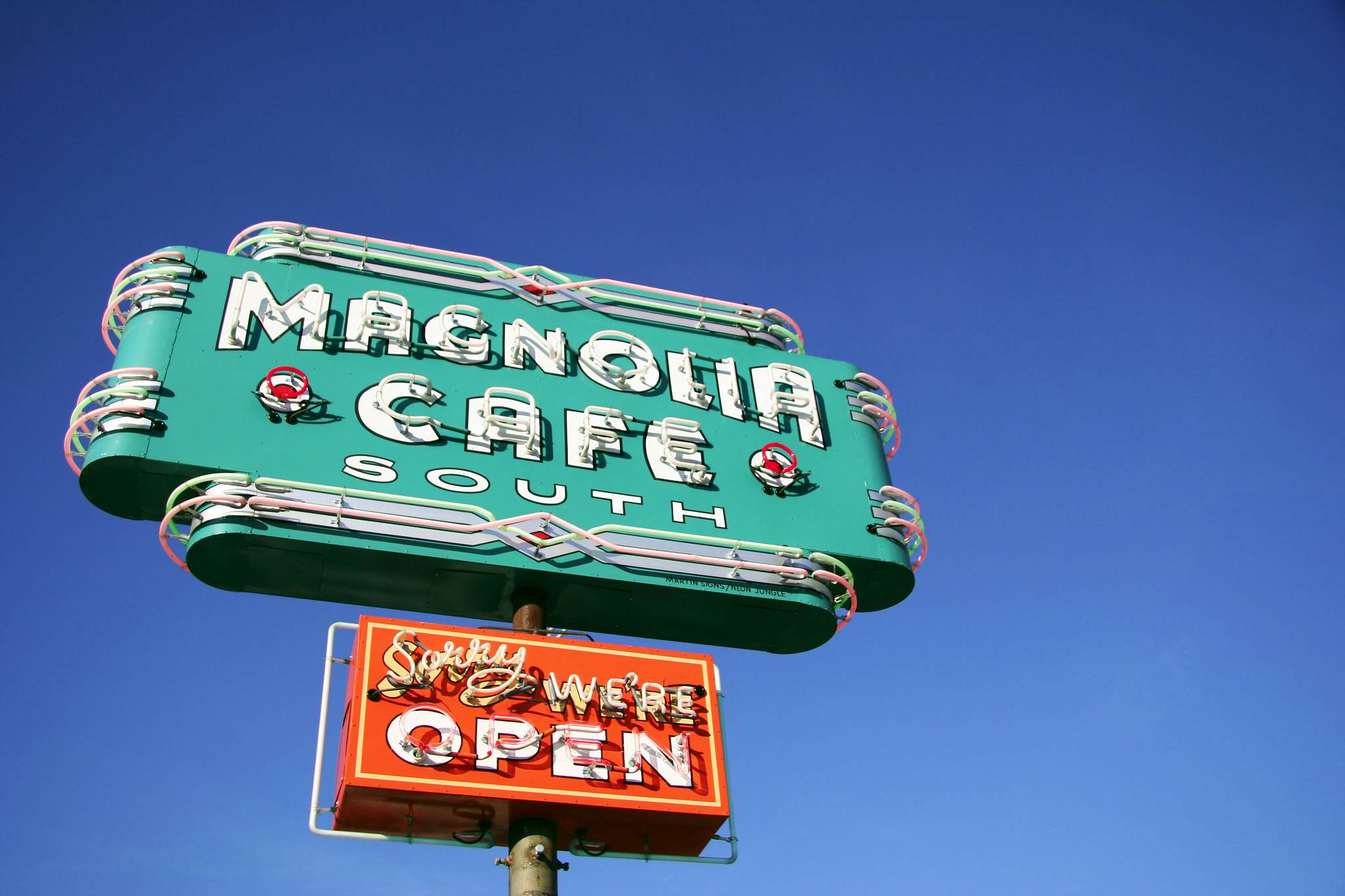 Turquoise neon sign that says Magnolia Cafe South over a smaller red neon sign that says Sorry we're open