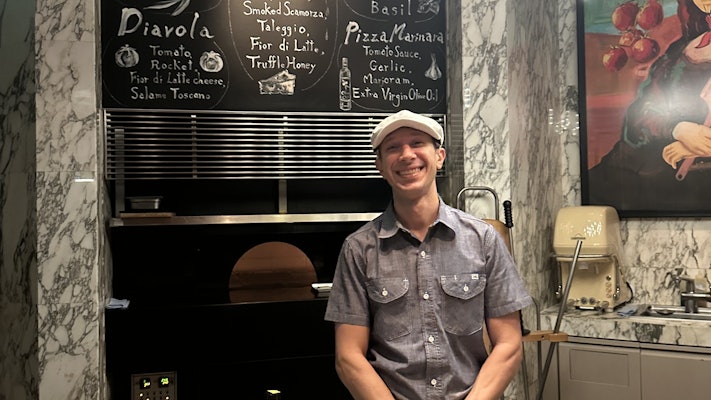 A pizzaiolo (pizza maker) smiles for a photo in front of his pizza oven