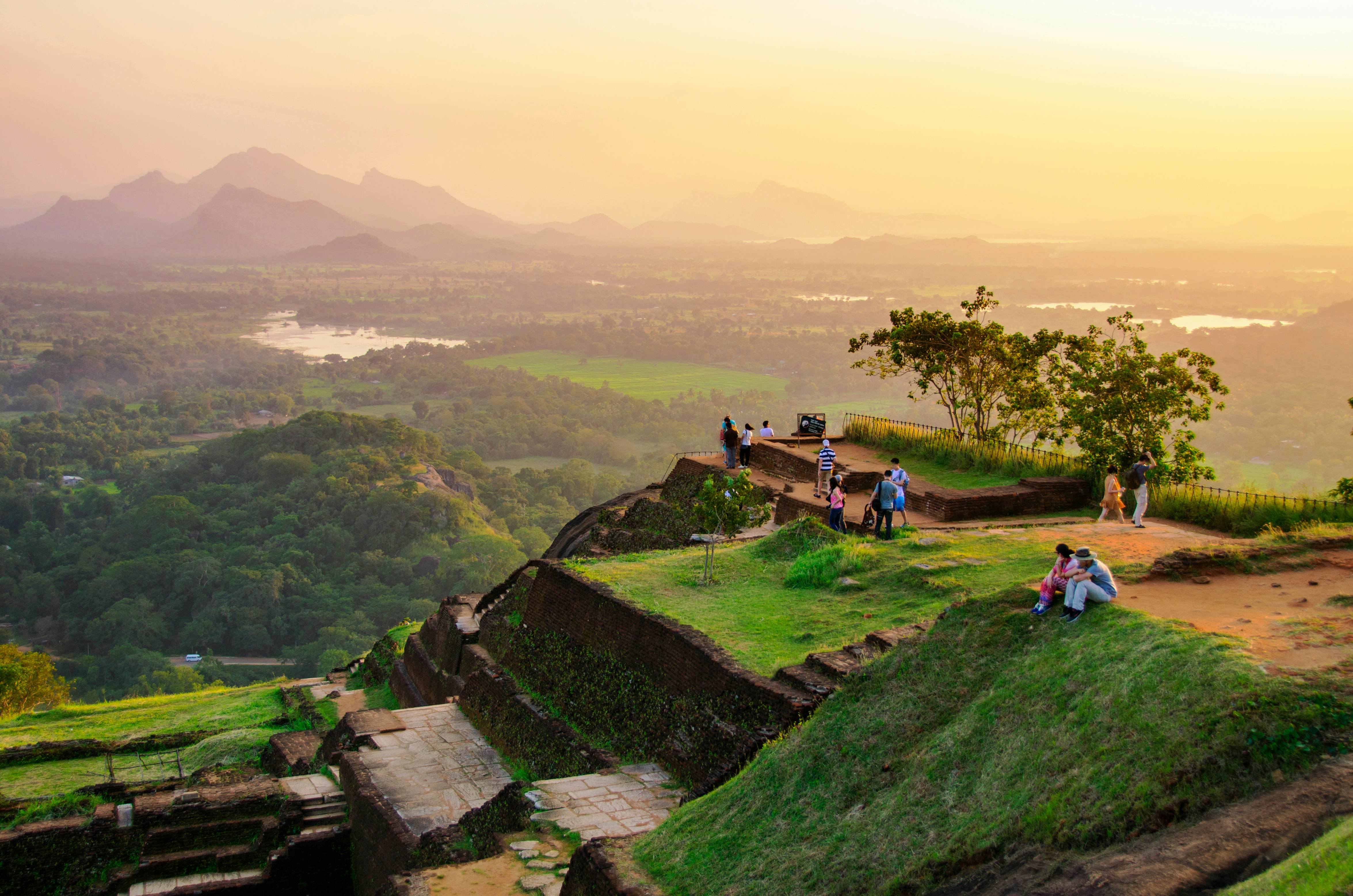 People sat on walls of an ancient site watching the sunrise over the surrounding landscape