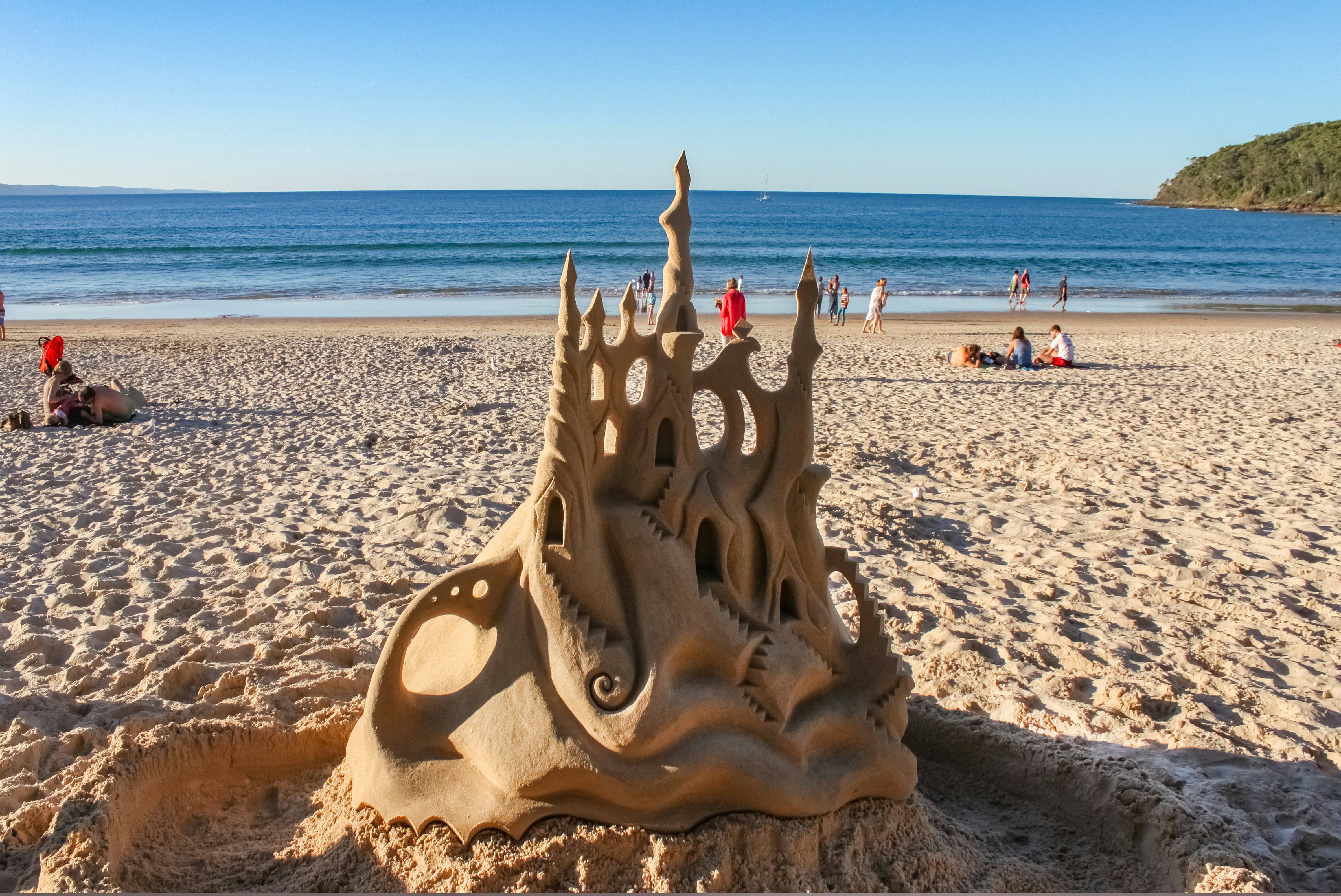 Fancy sand castle with moat in foreground on beach with people enjoying the sand and sea behind at Noosa Heads