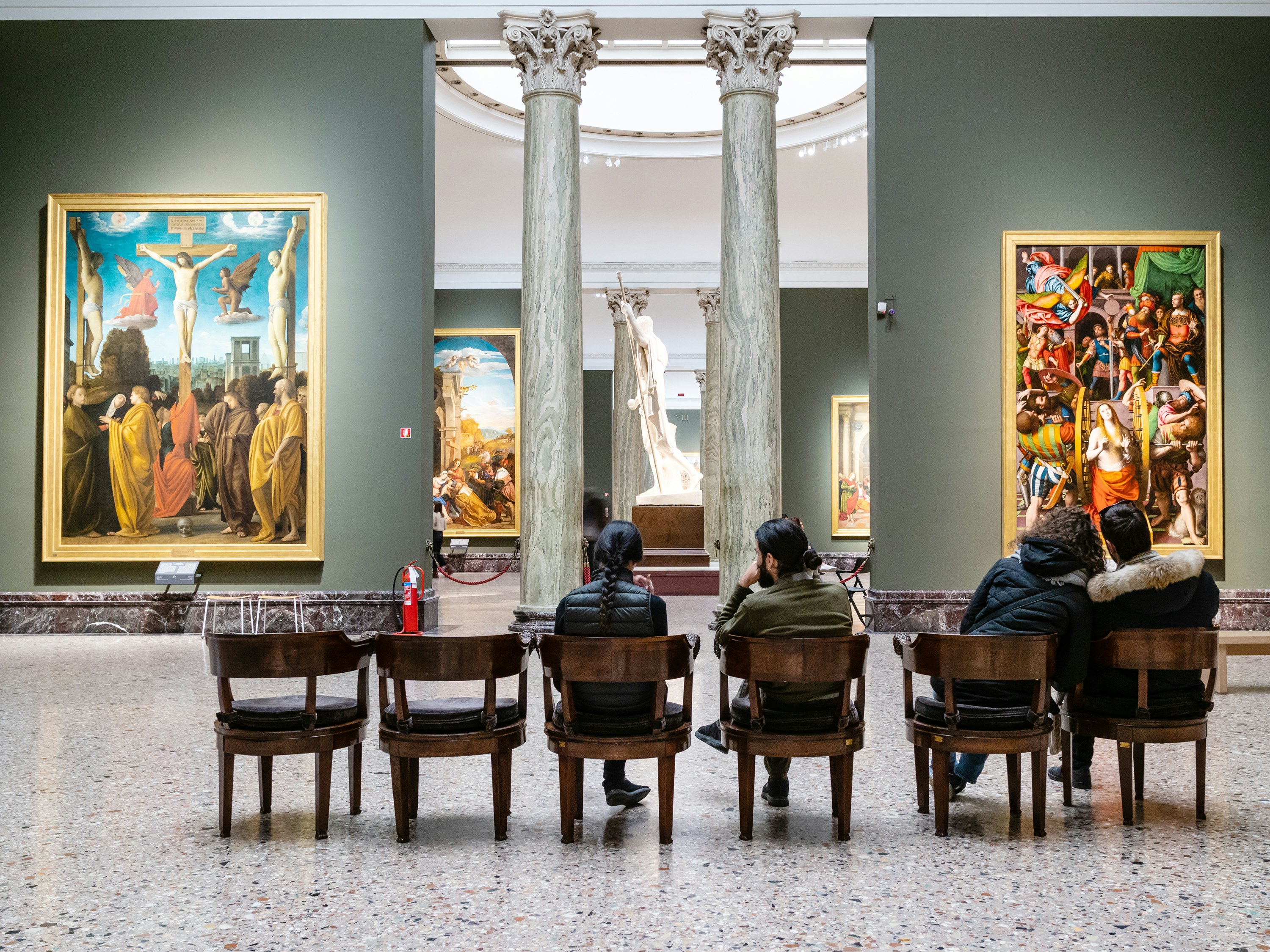 People sat in chairs in an art gallery gazing at the paintings and sculptures.