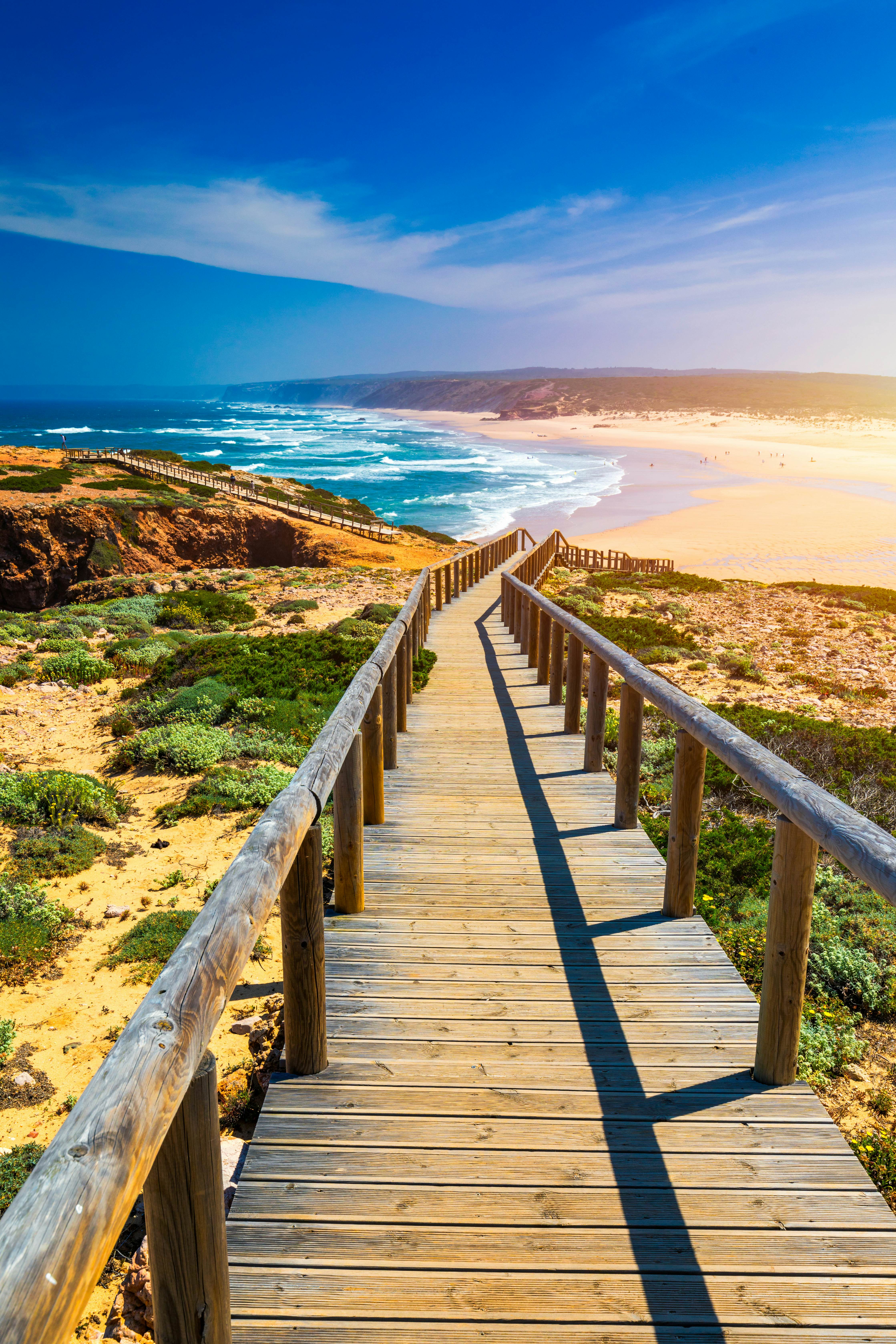 A wooden boardwalk leads down to a sandy beach