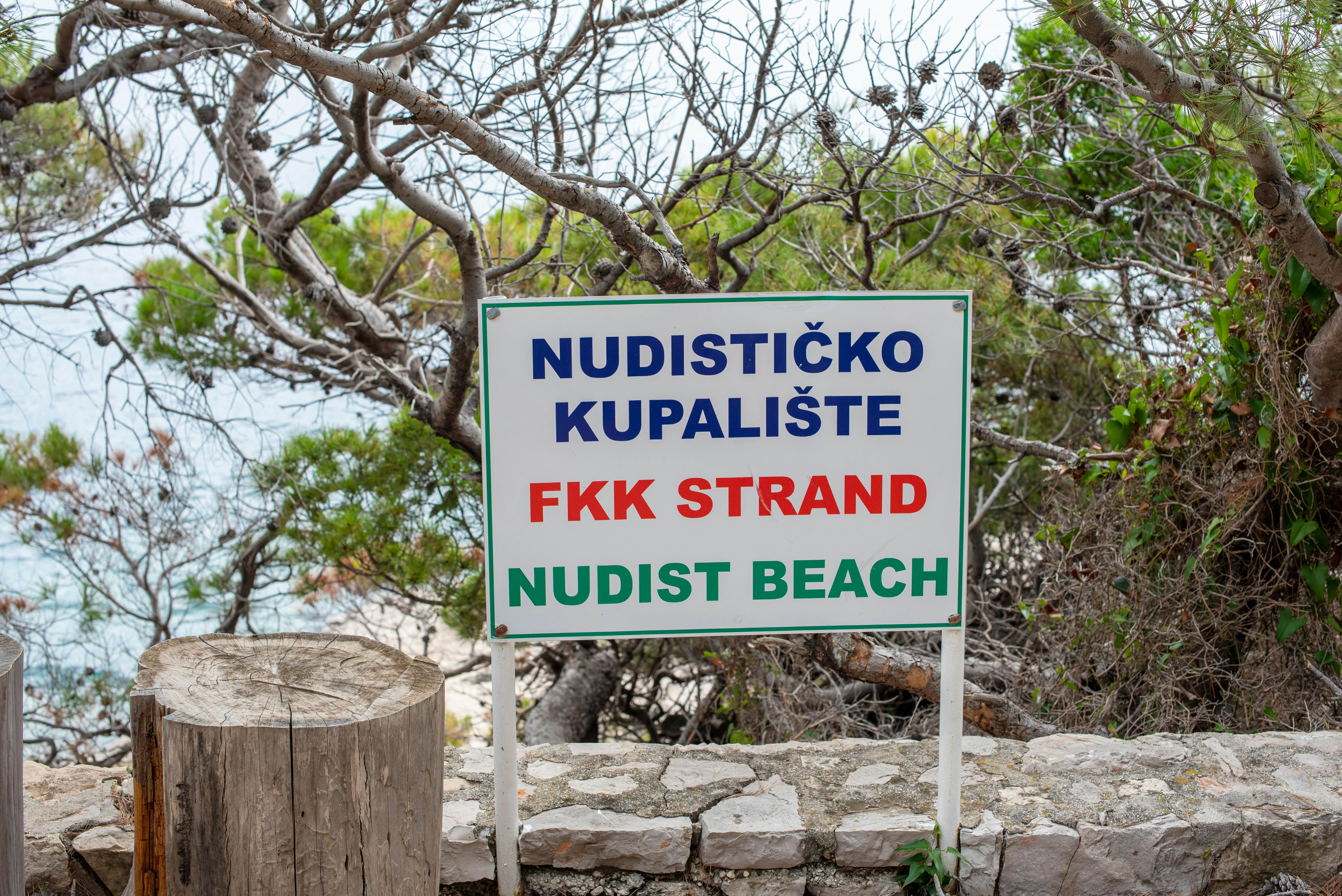 A sign indicates a nudist beach beyond the trees directly behind the sign.