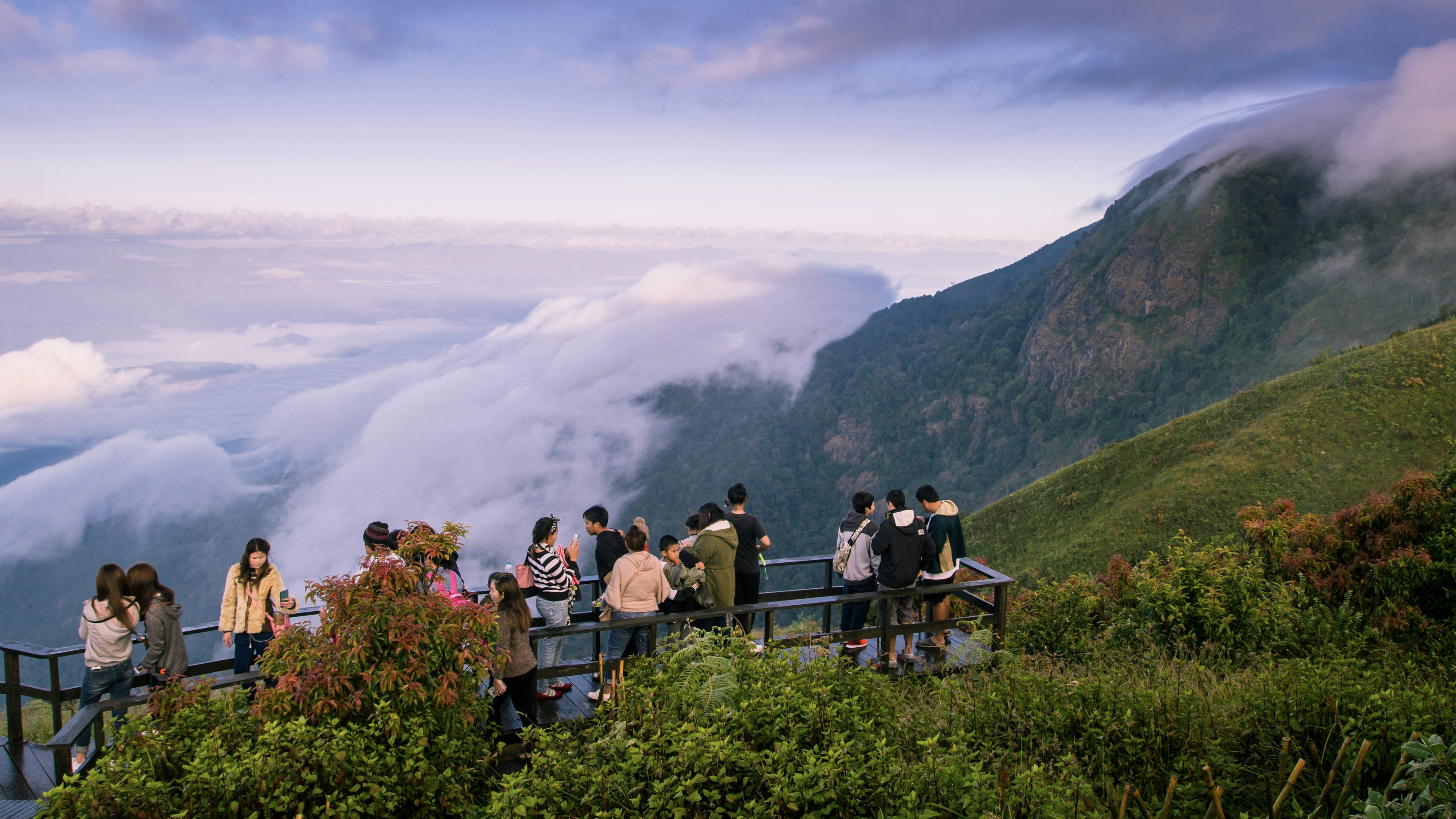 Tourists stand on an overlook to catch sweeping views of grassy mountains