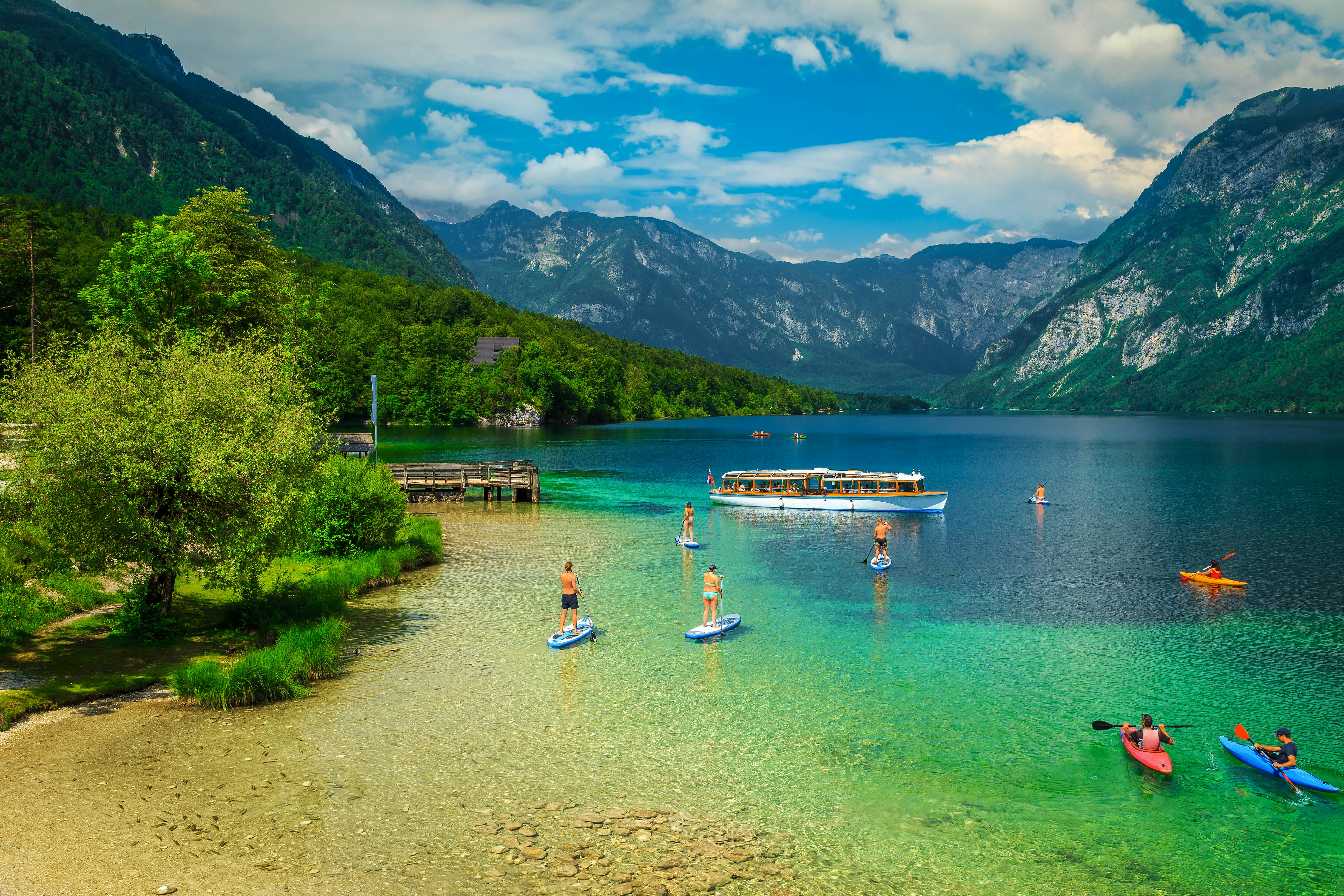 Healthy sporty friends exercising on the colorful sup boards. Active friends kayaking on the lake Bohinj, Ribcev Laz, Slovenia, Europe