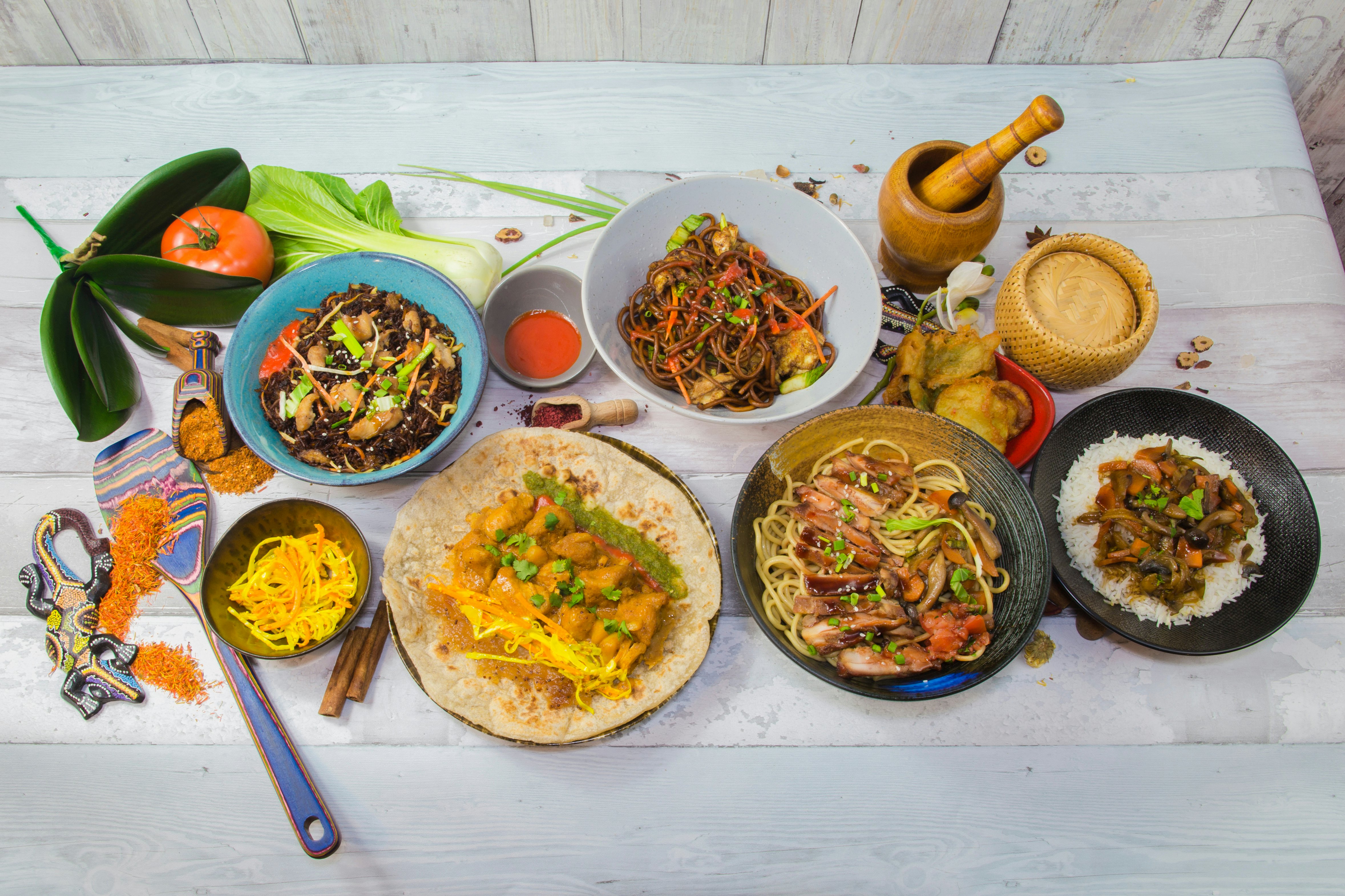 An overhead view of several dishes laid out on a table, featuring fresh fish and colorful produce as ingredients.