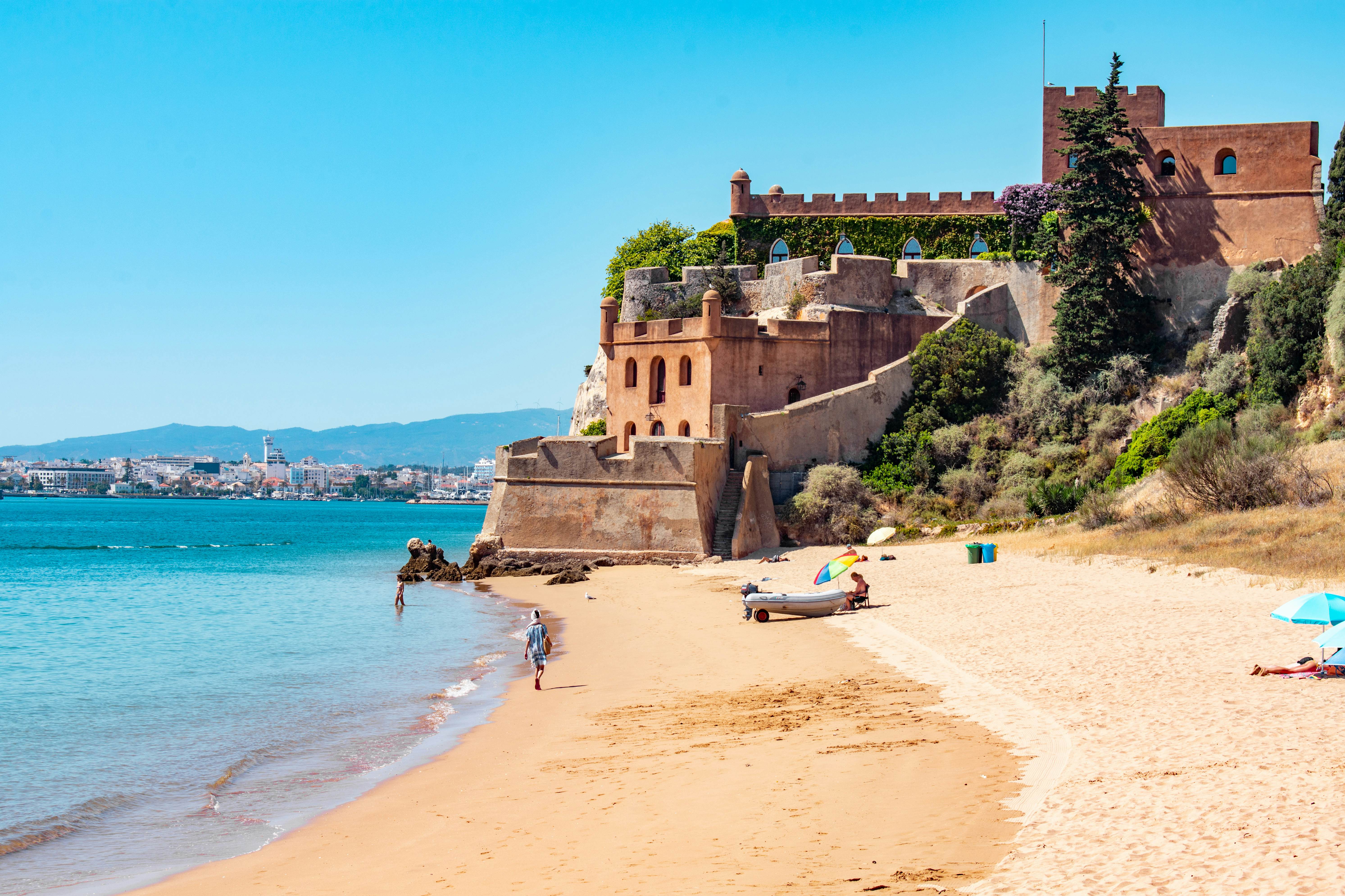 People walking along a beach with a castle in the distance.