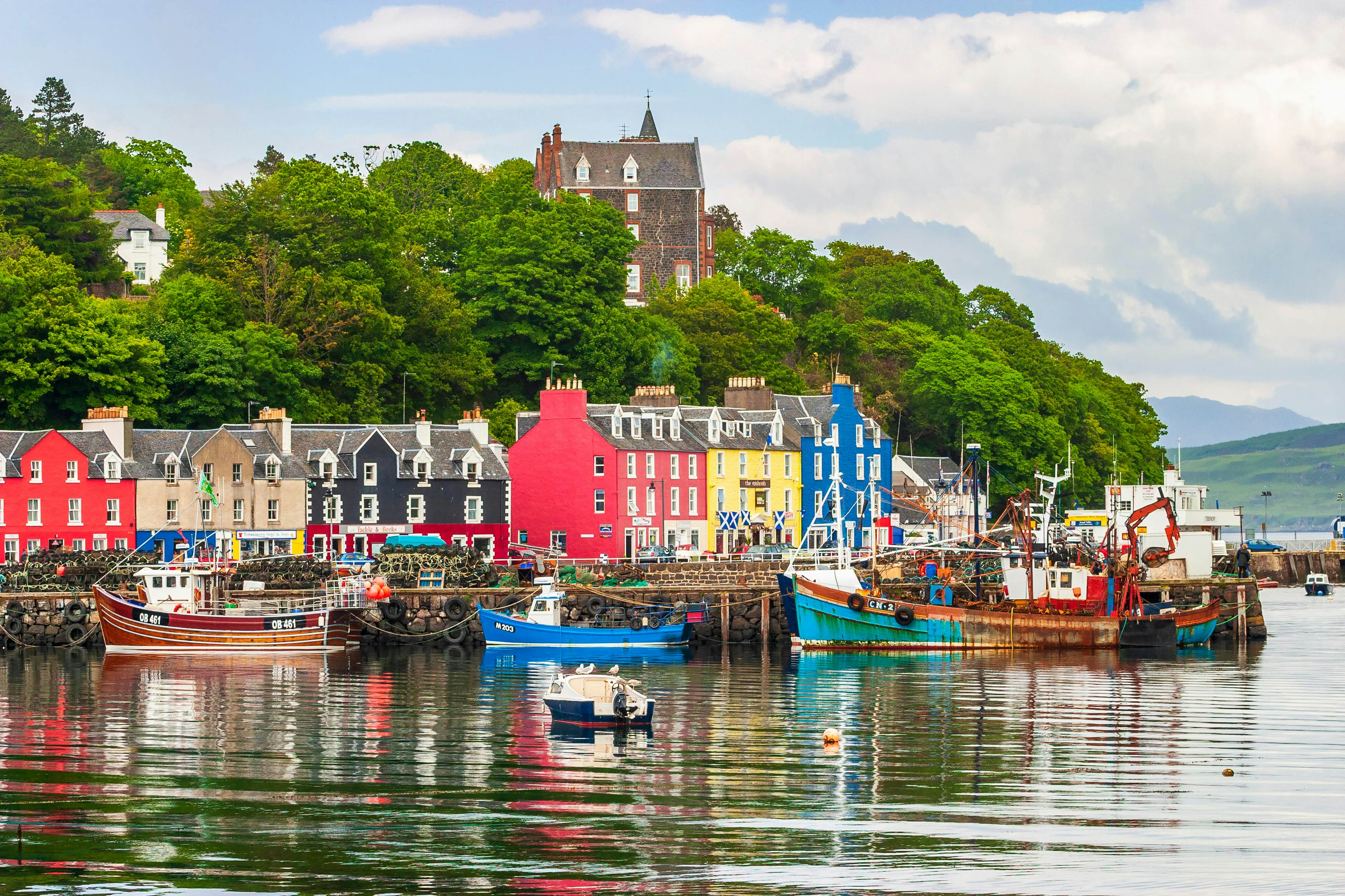 Boats in a small harbor lined with cottages painted in bring red, yellow and blue