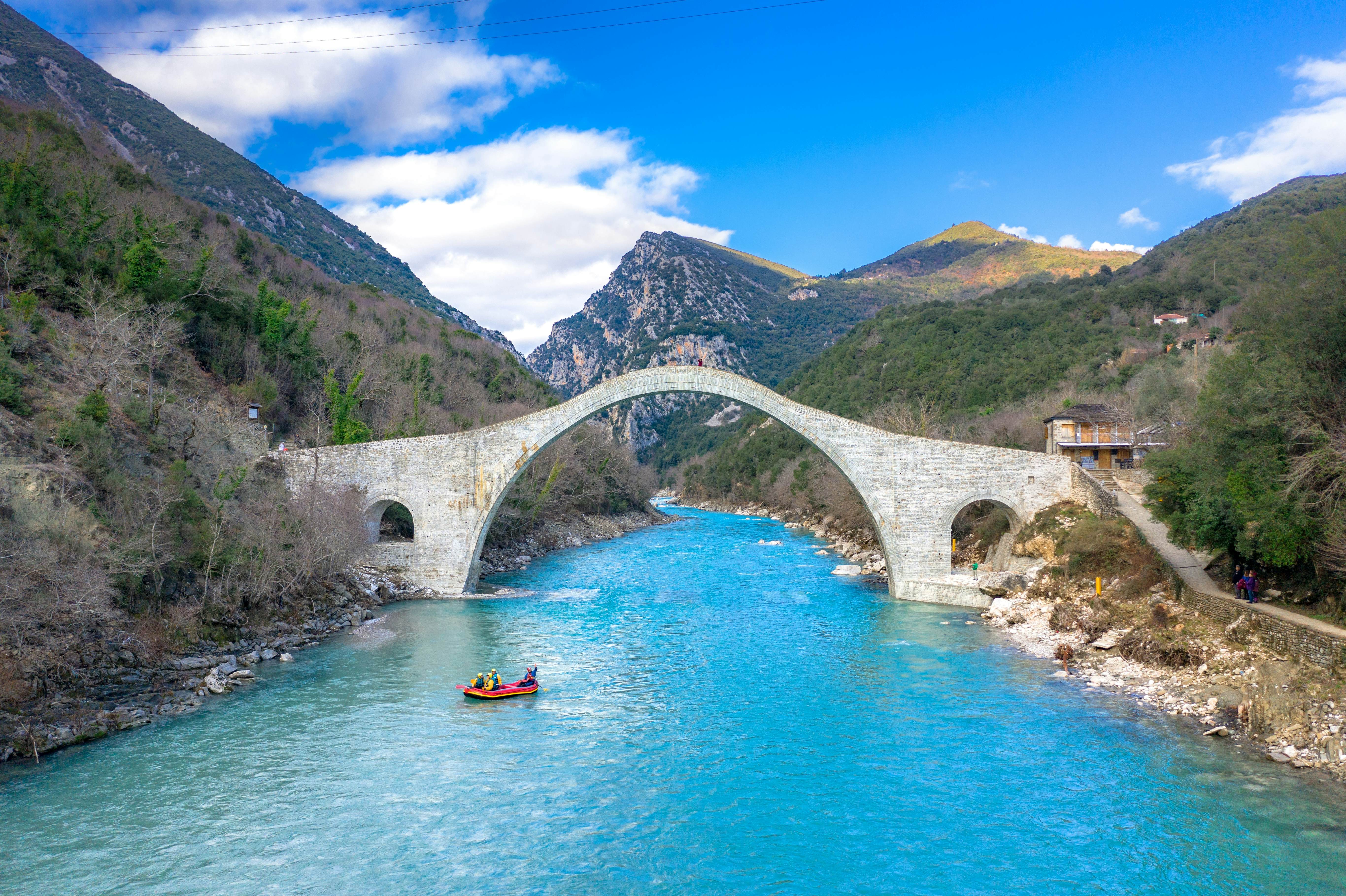 A raft underneath a stone bridge over the bright blue Arachthos river in Epiros, Greece