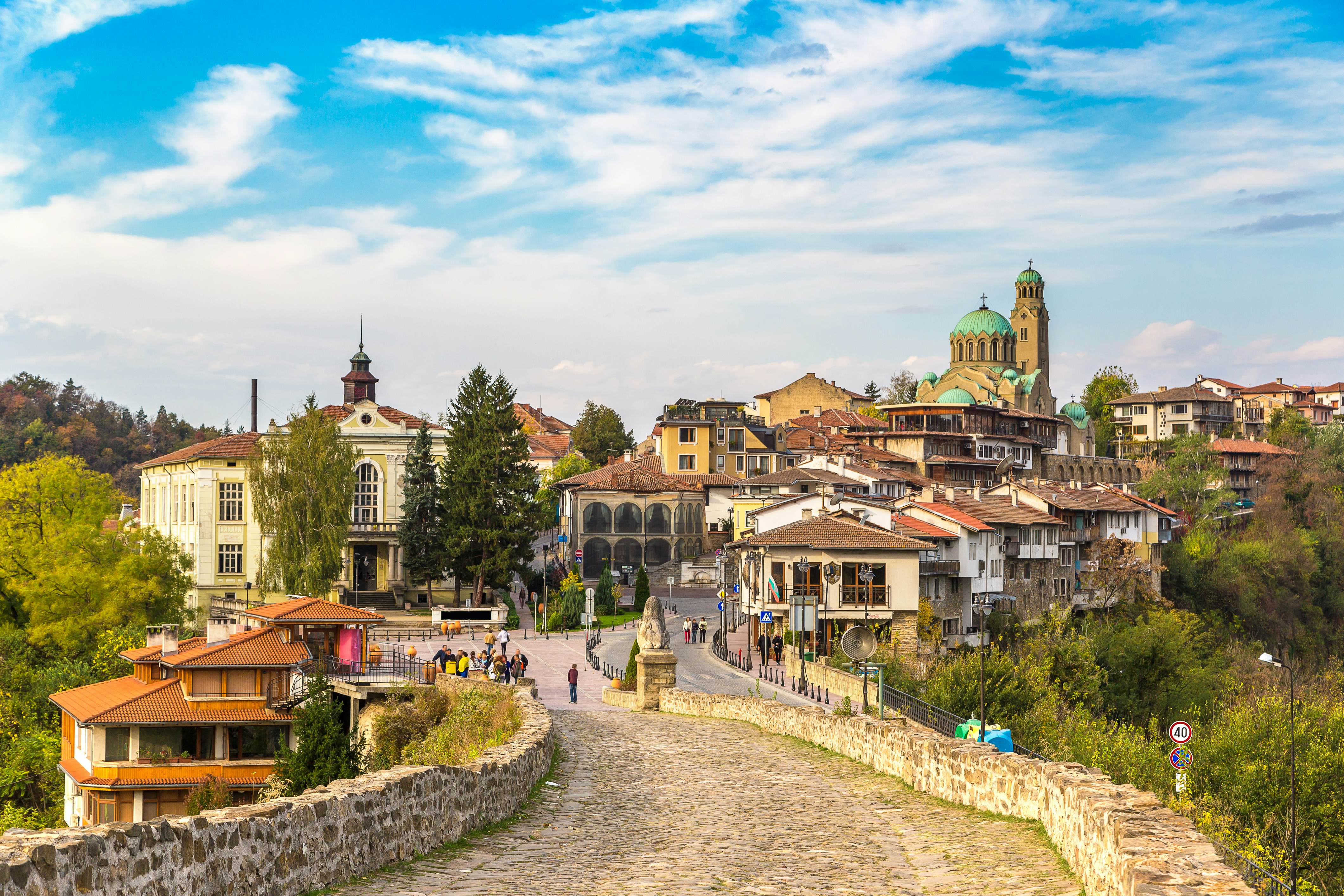 A cobbled pathway leads to a hillside town with a green-domed church