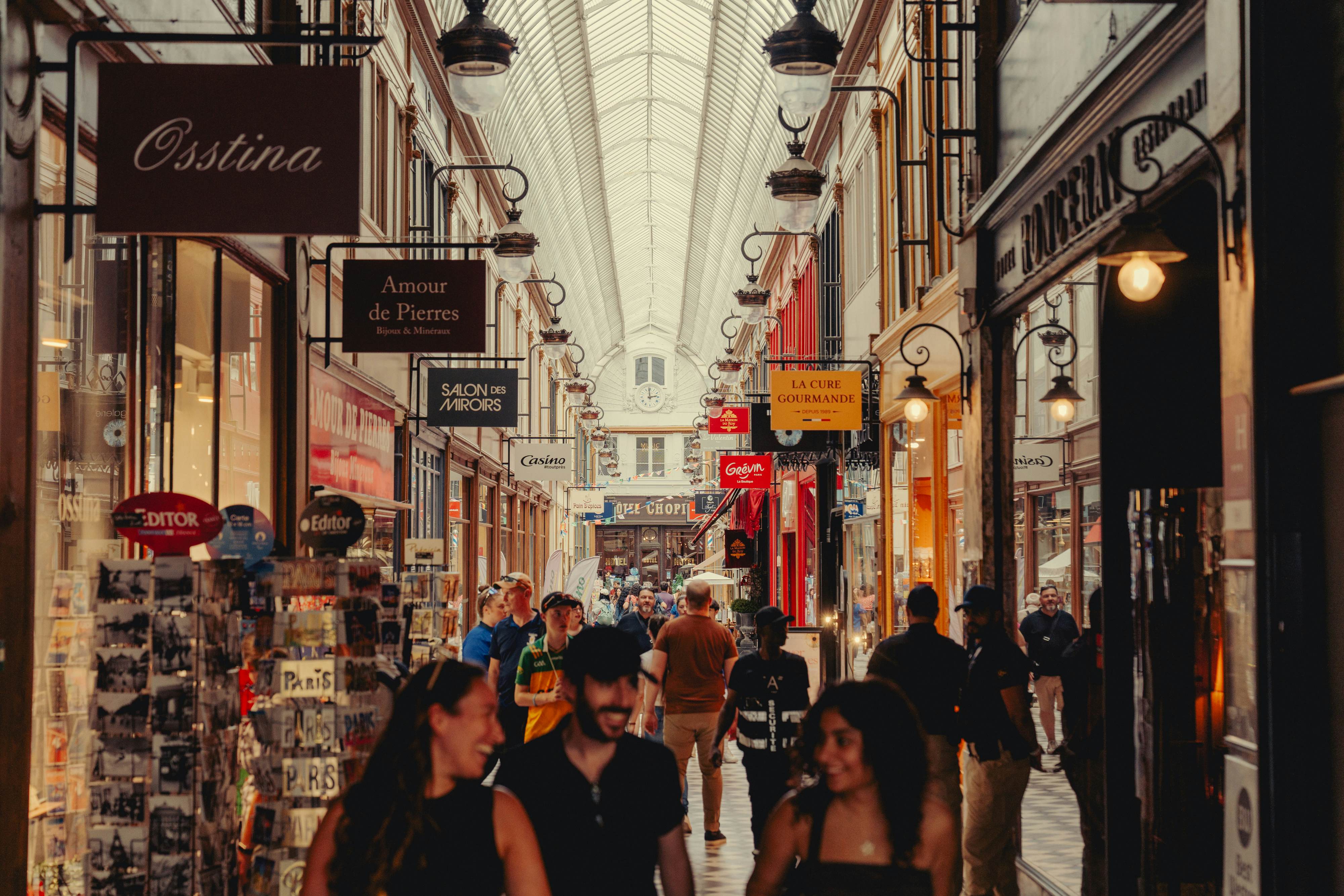 People smile as they walk through a covered passageway featuring an arcade of small shops.