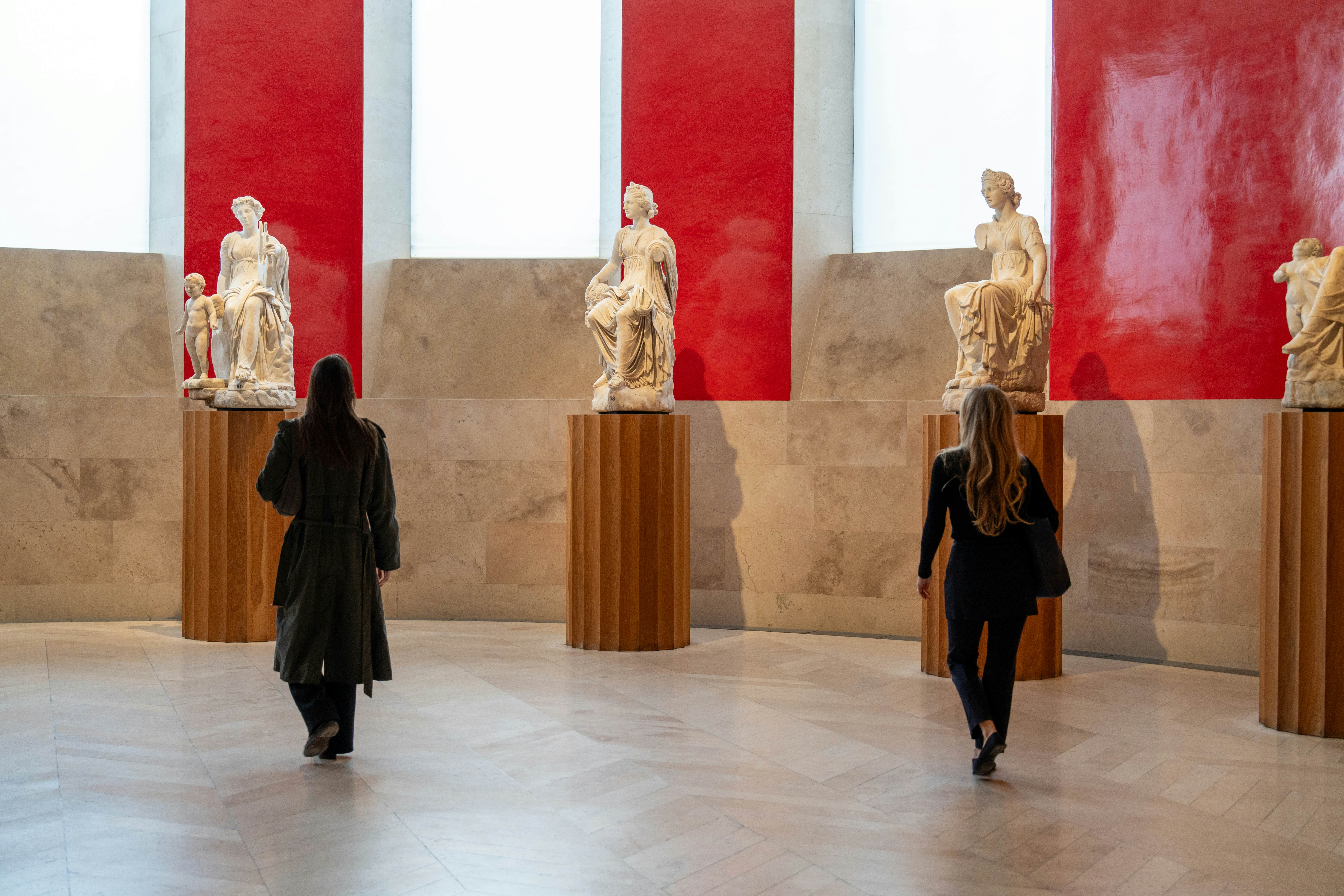 Two women admiring sculptures standing on plinths in a museum.